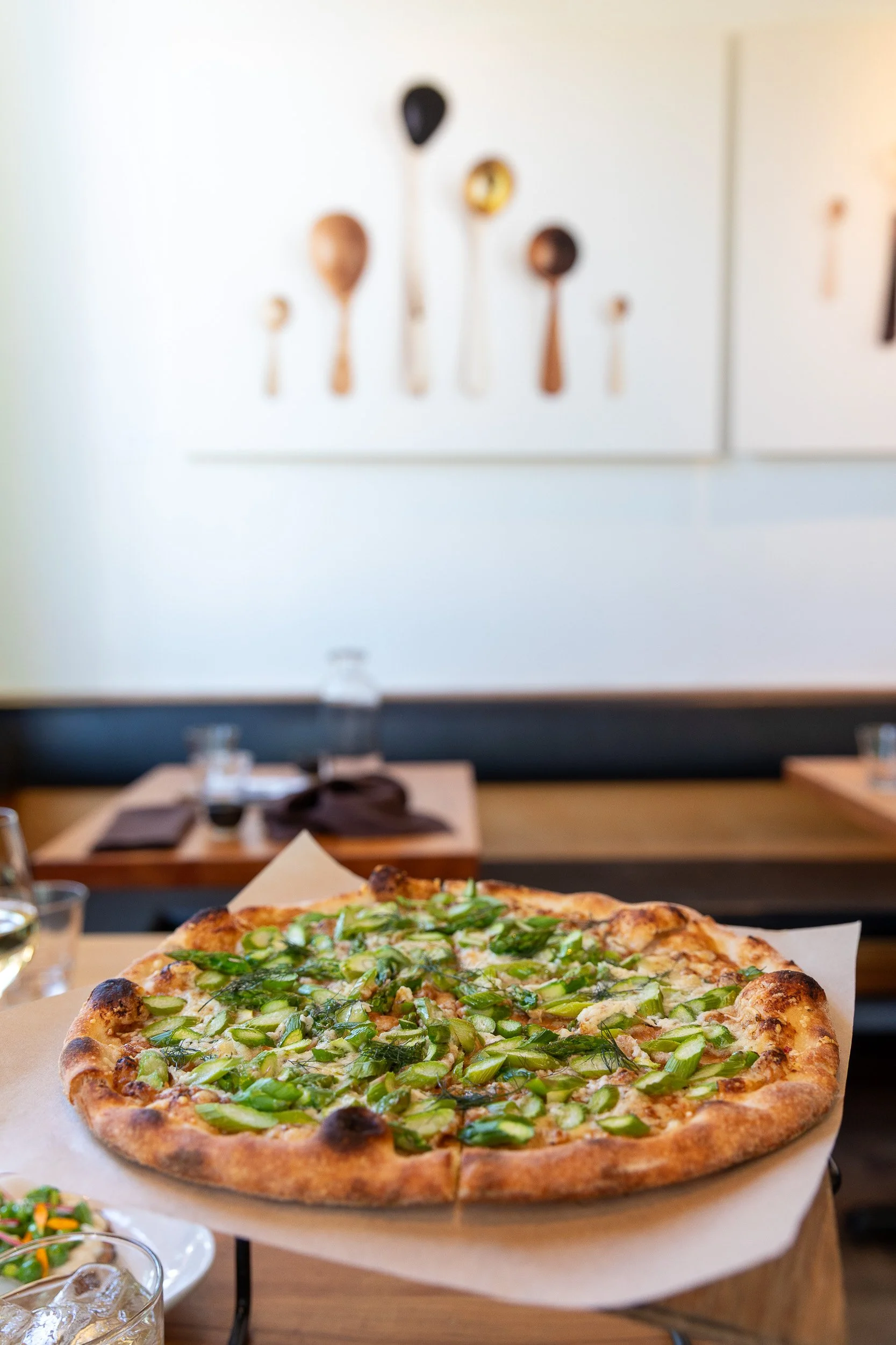 A pizza topped with green vegetables, likely scallions or green onions, on a pizza tray in a restaurant setting.