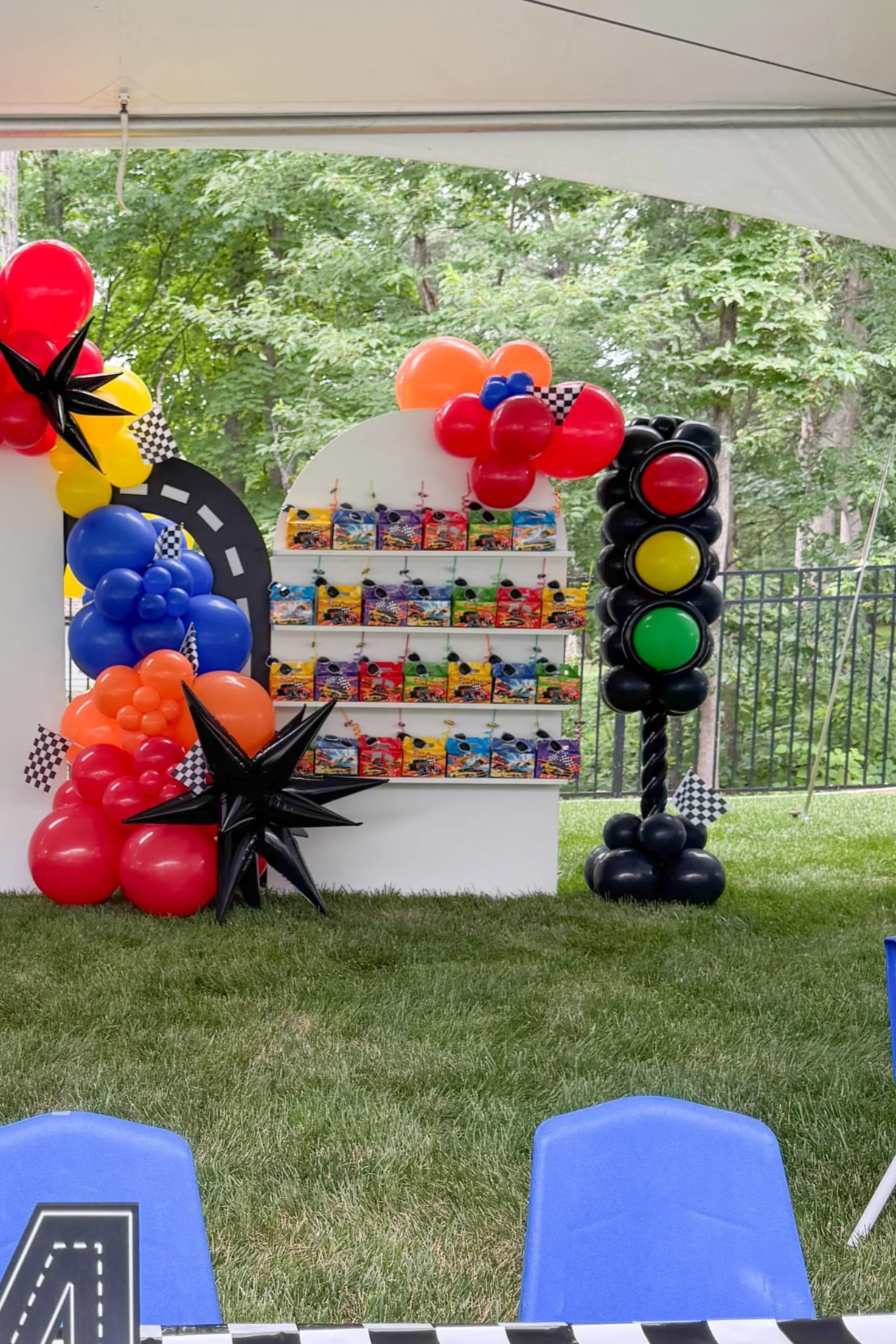 Colorful race car themed balloons and a display of miniature toy cars arranged on a white board at an outdoor event.