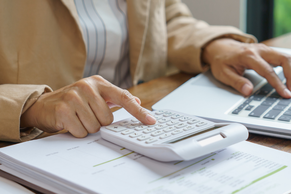 woman using her laptop and a calculator with a stack of papers