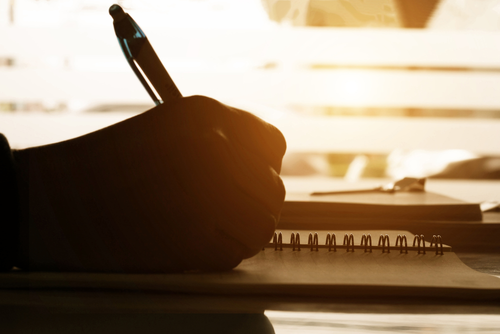 Person writing in a notebook with a pen with warm glow backlighting