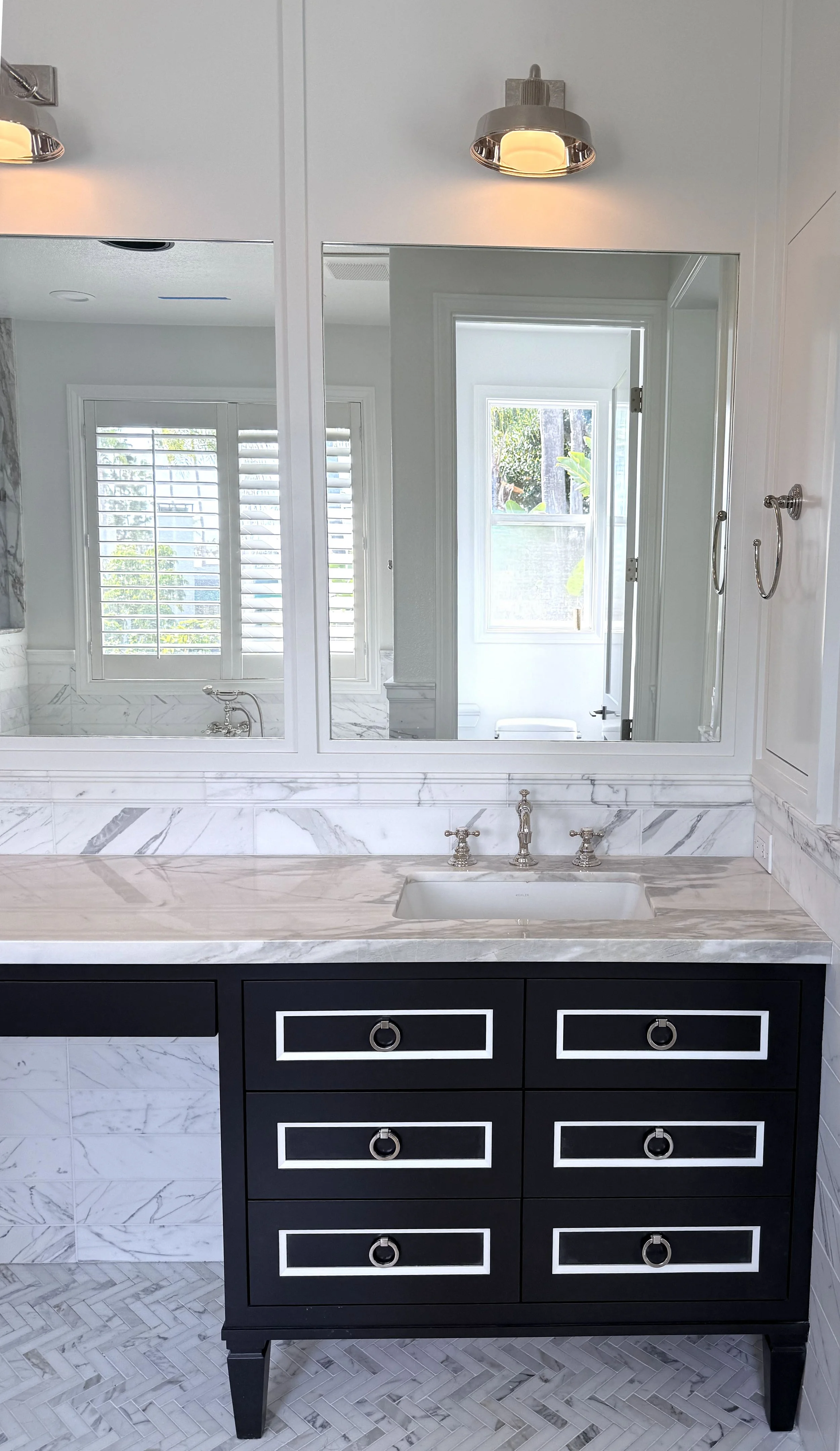 Bathroom vanity with black drawers, marble countertop, and large mirror, reflecting window and shower in background.