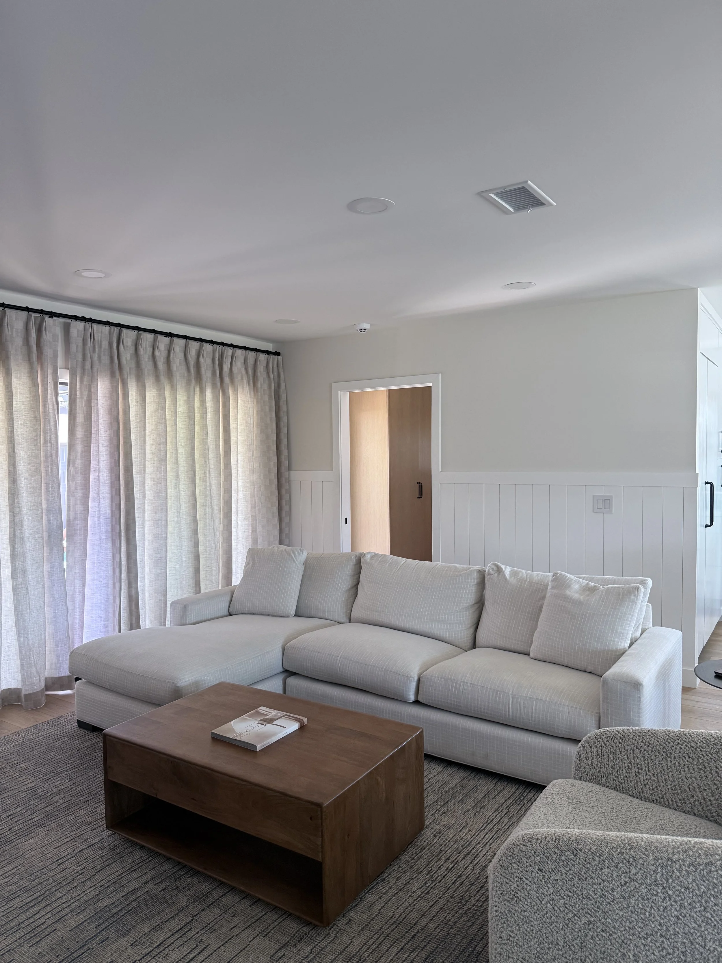 Comfortable family room with sectional sofa, layered window treatments, area rug, and warm wood coffee table.