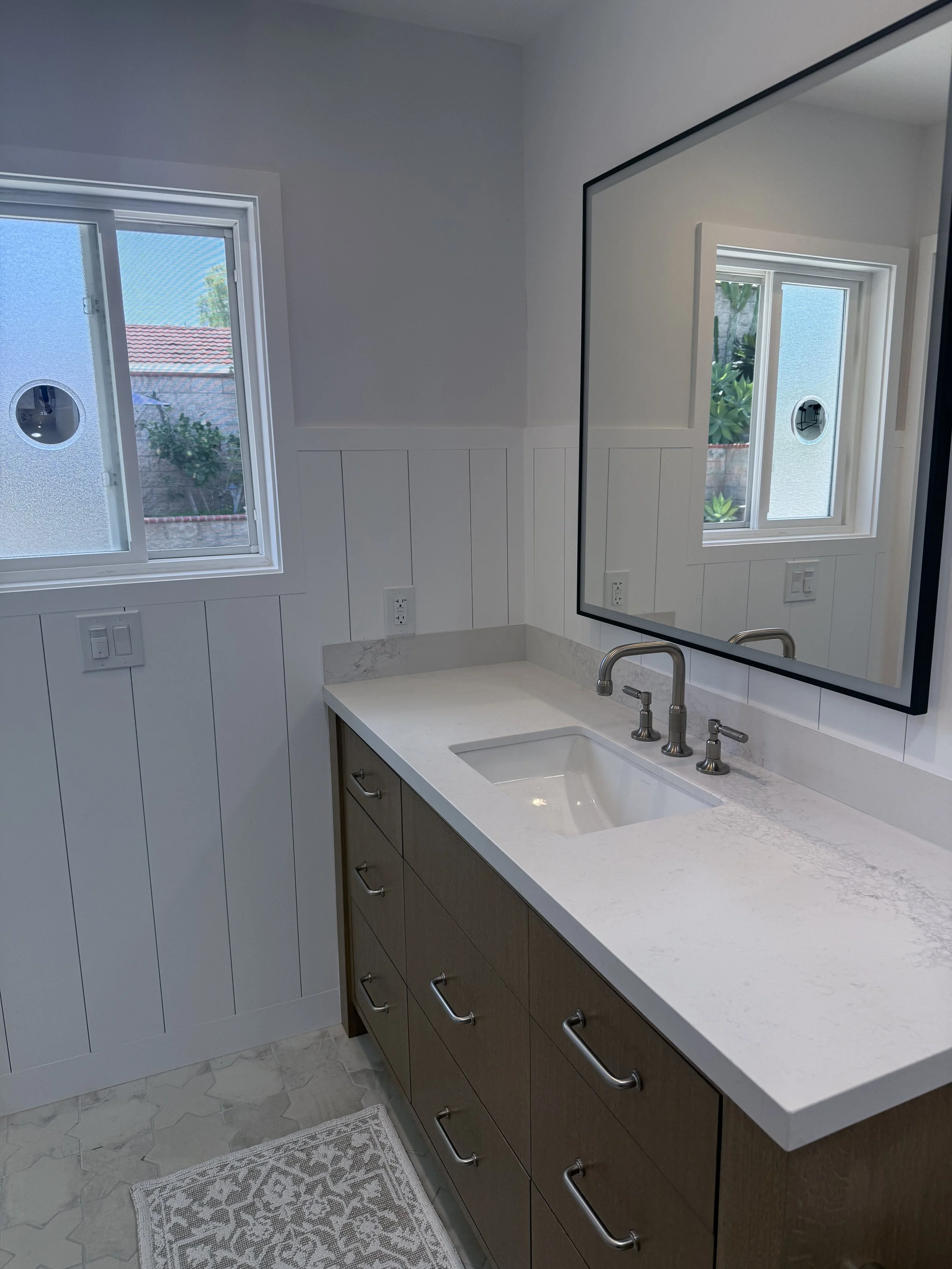 Custom bathroom vanity with quartz countertop, wood cabinetry, framed mirror, and modern lighting.