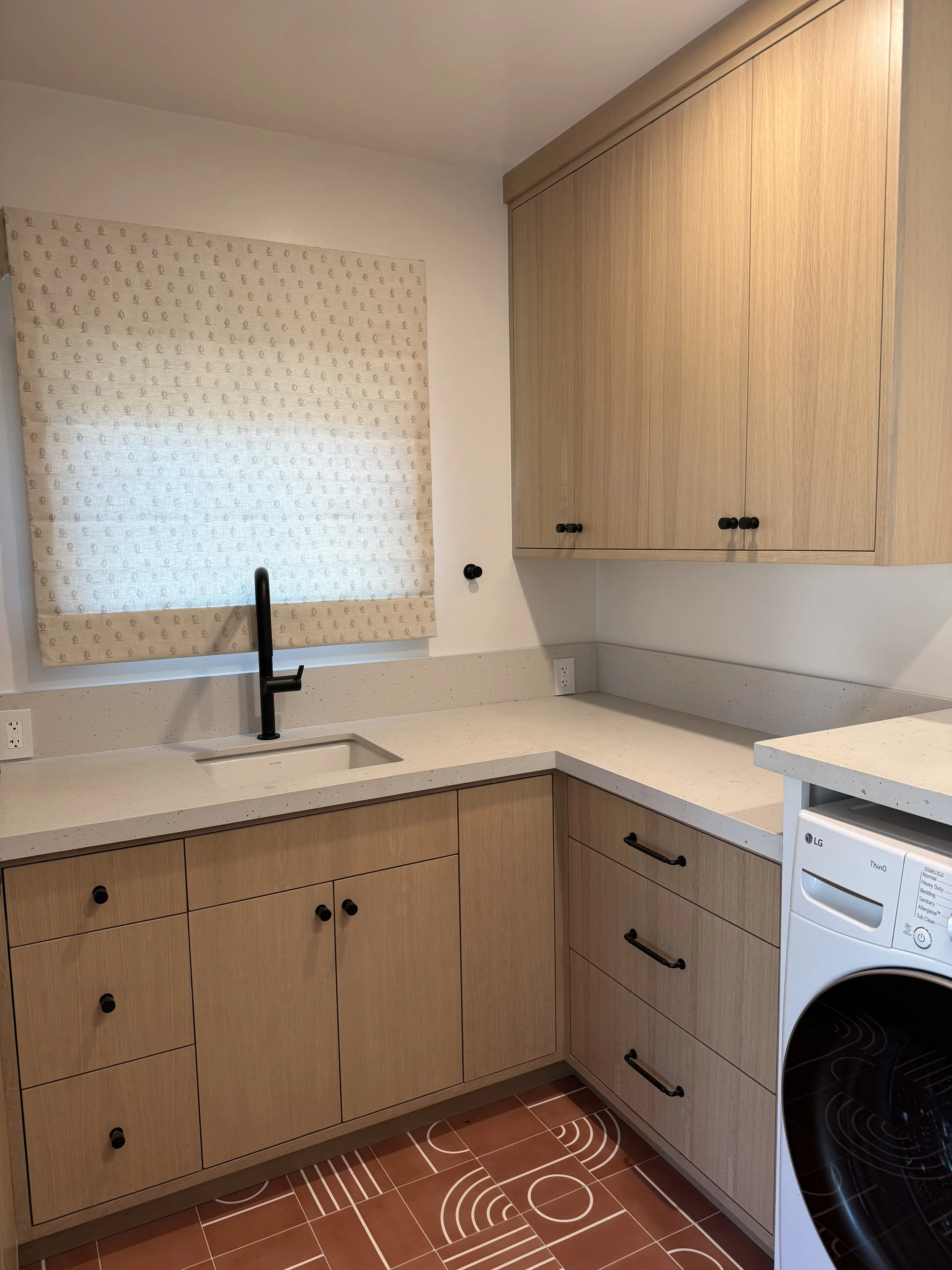 Laundry room with white oak cabinetry, white countertops, black fixtures, and patterned terracotta floor tile.