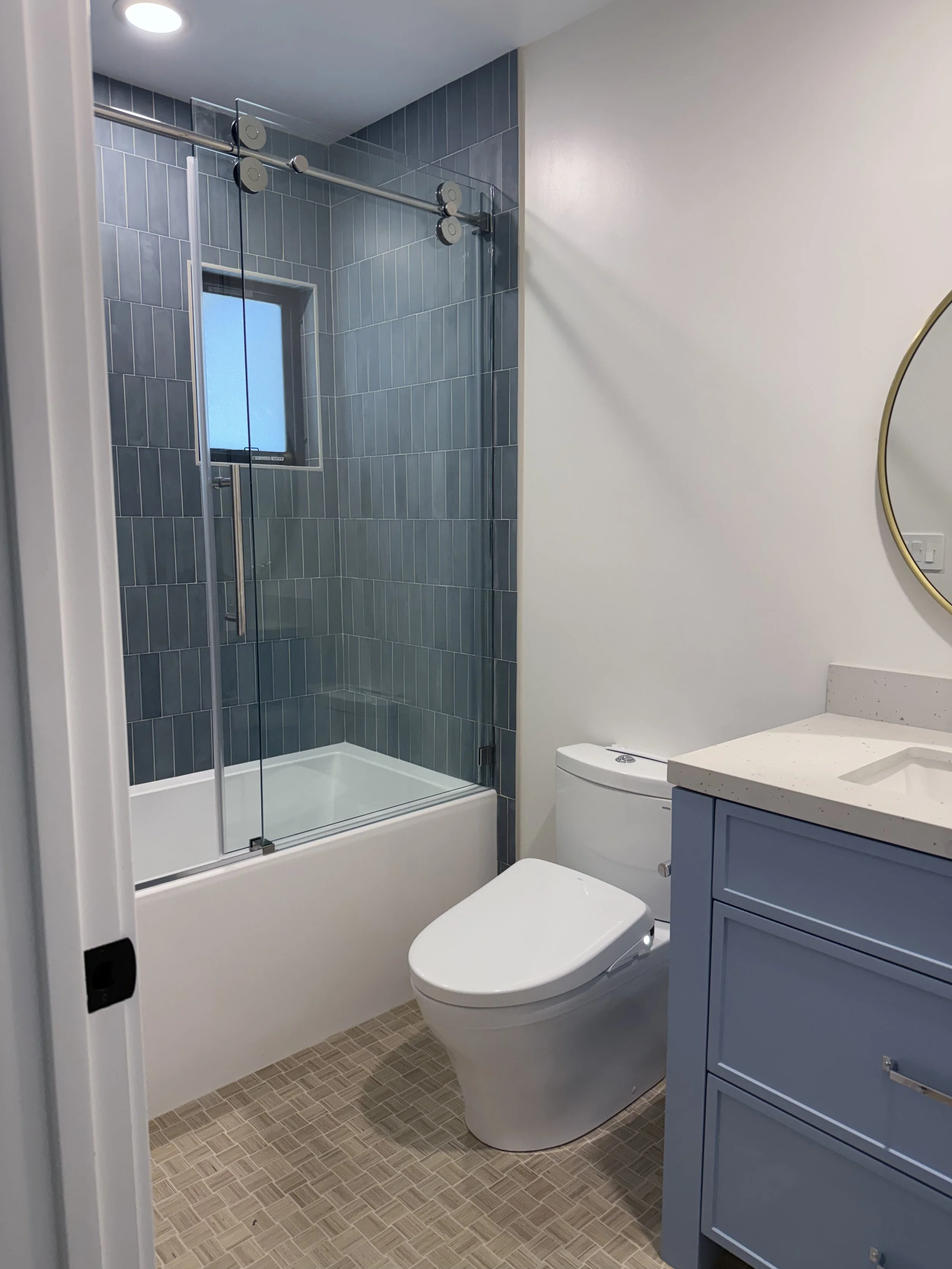 Remodeled bathroom with blue vanity, bathtub surrounded by blue handmade-look tile, and terrazzo-style flooring.