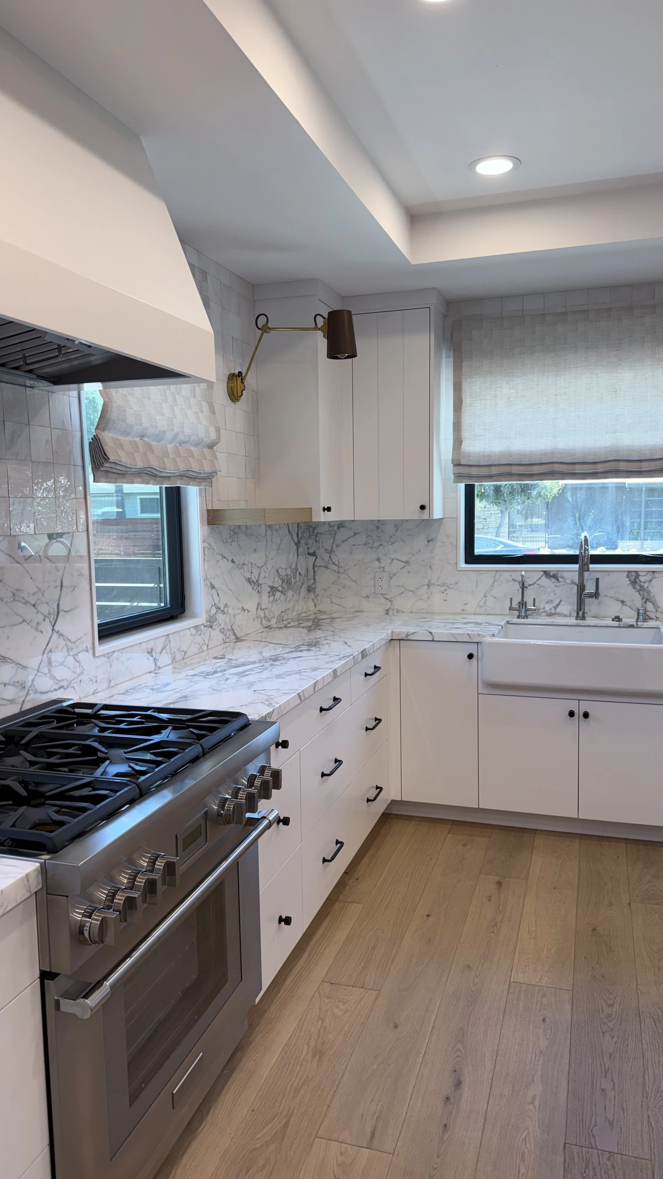 Custom white kitchen with professional-style range, natural stone backsplash, brass accents, and light wood flooring.
