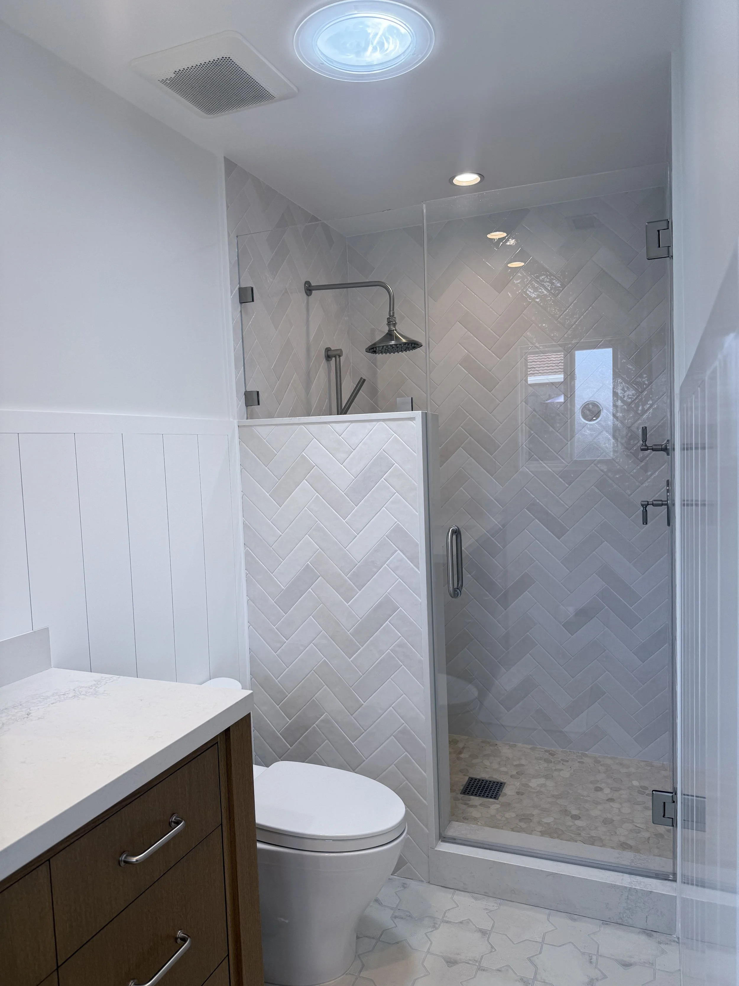 Primary bathroom remodel with custom vanity, white countertop, walk-in shower, and porcelain tile flooring.