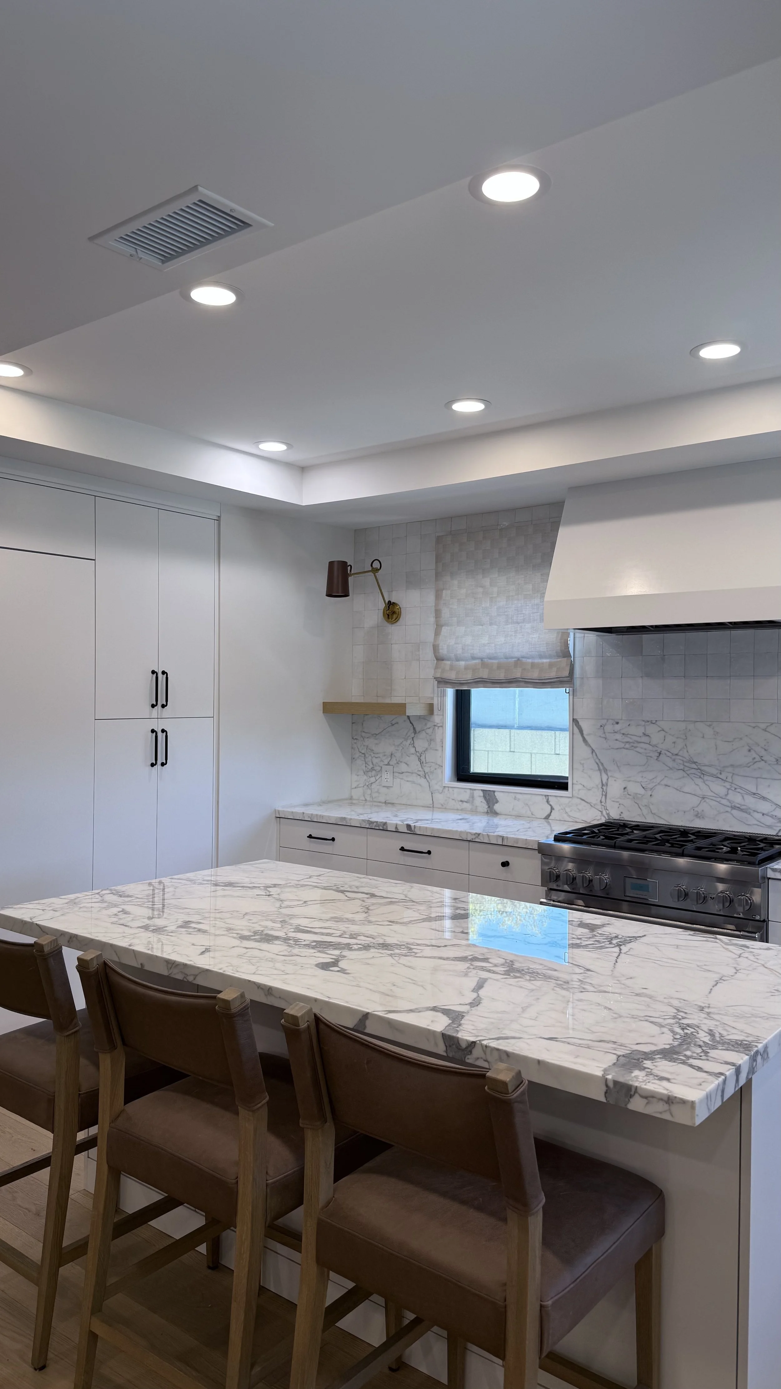 Custom East Long Beach kitchen with white cabinetry, natural stone countertops and backsplash, and a large waterfall island.