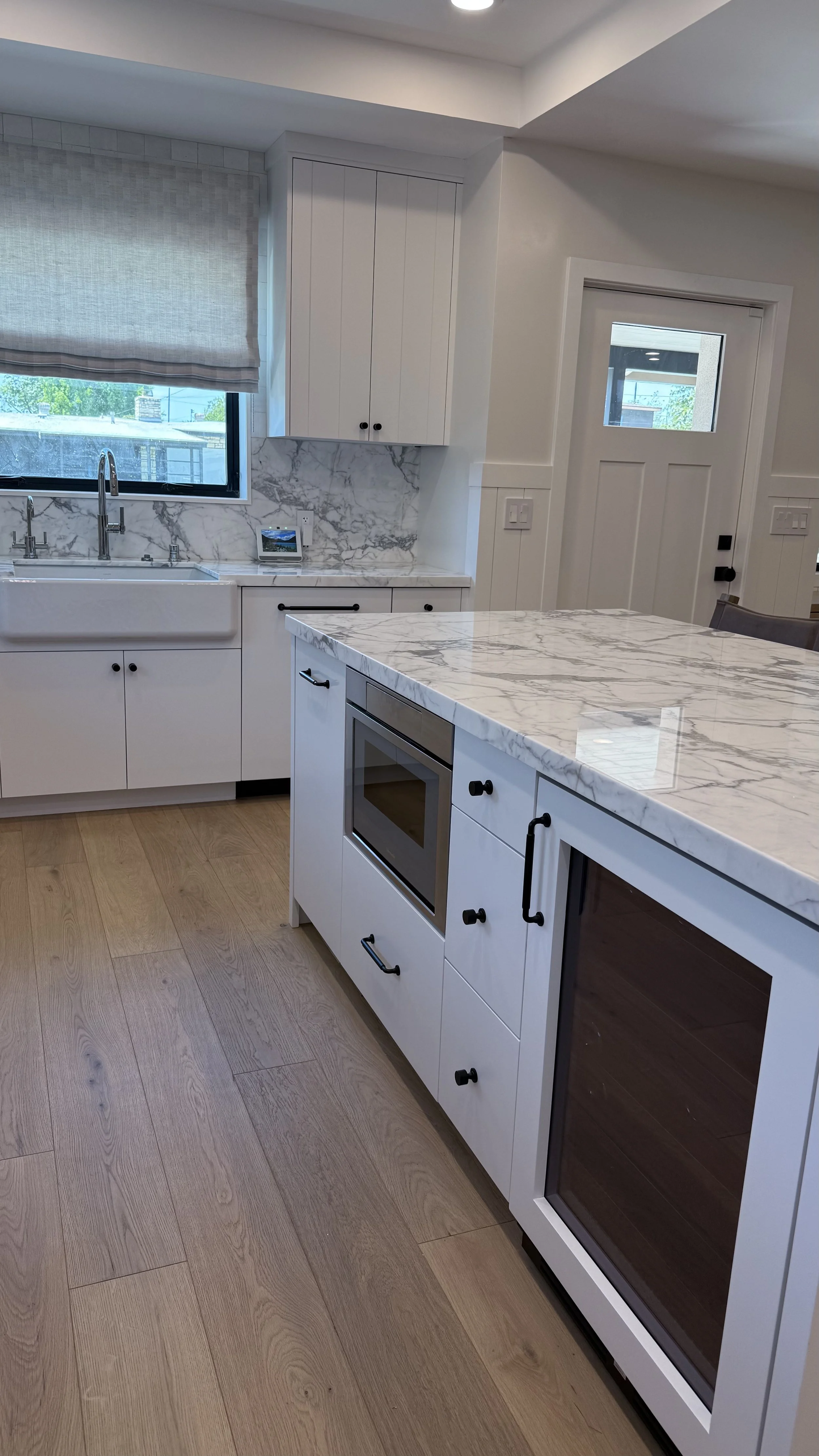 Large kitchen island with waterfall stone countertop, built-in microwave, beverage refrigerator, and custom cabinetry.