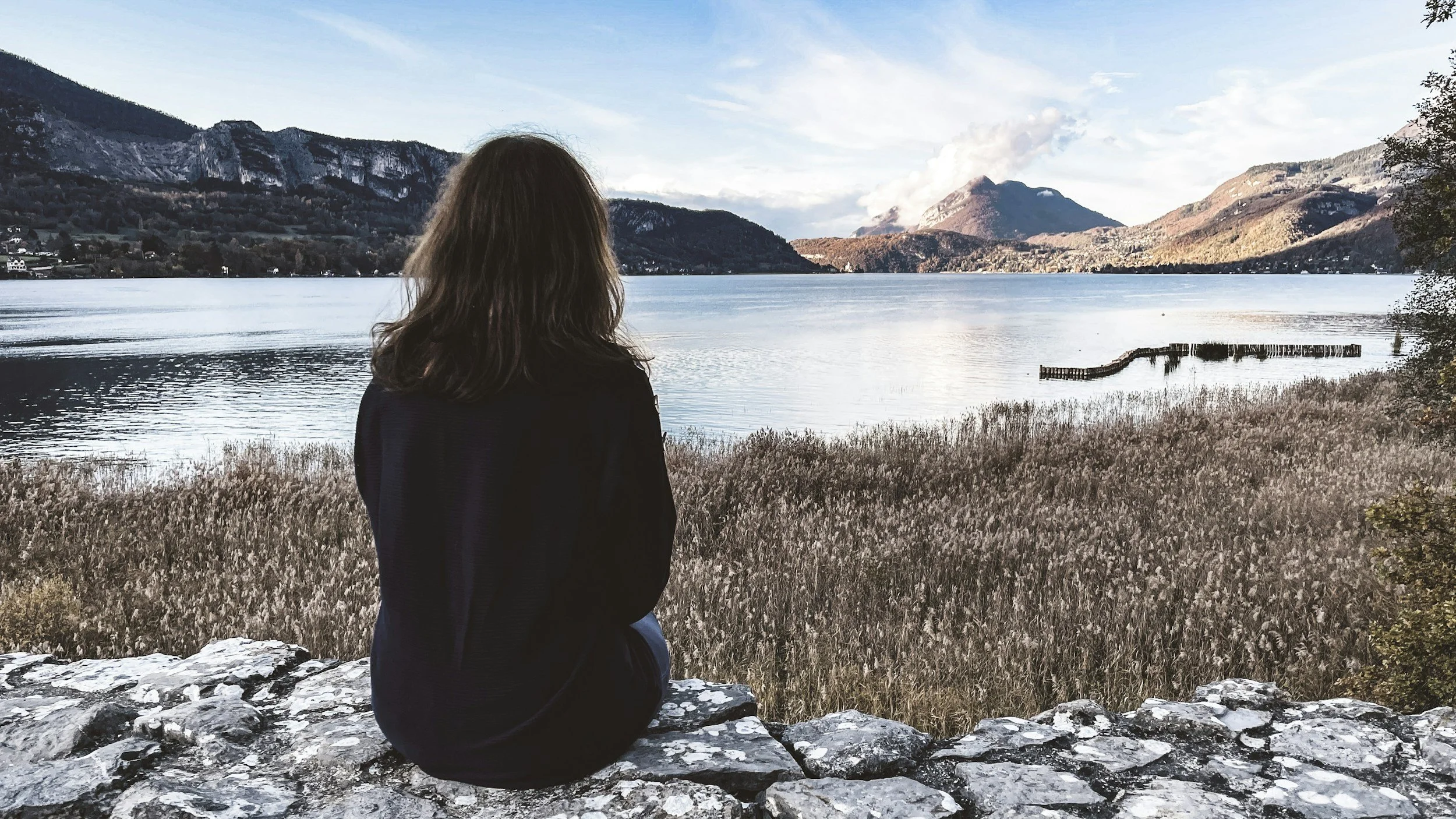 Woman sitting alone overlooking a lake and mountains representing quiet reflection and identity in the empty nest season