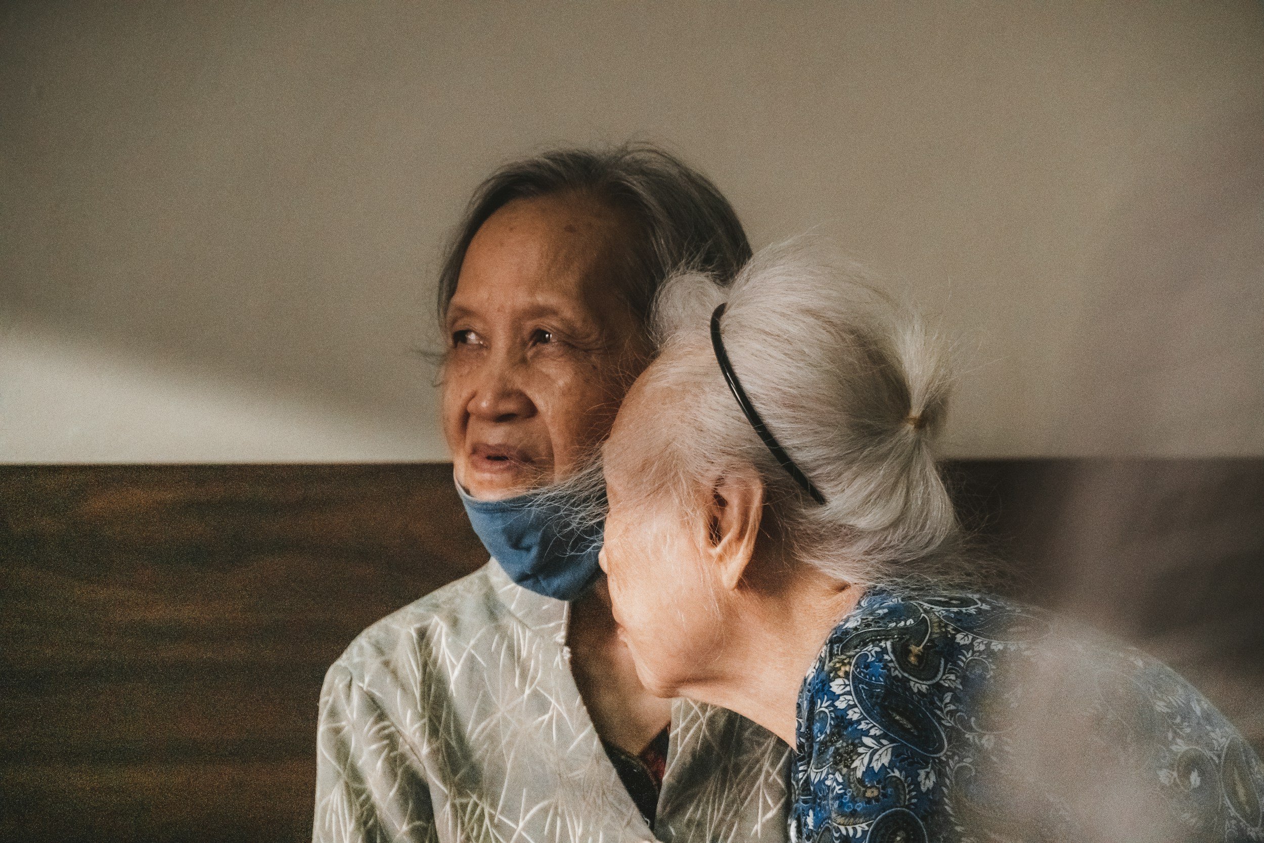 Older woman wearing a mask caring for an aging person representing the caregiver role and identity transition in the empty nest season