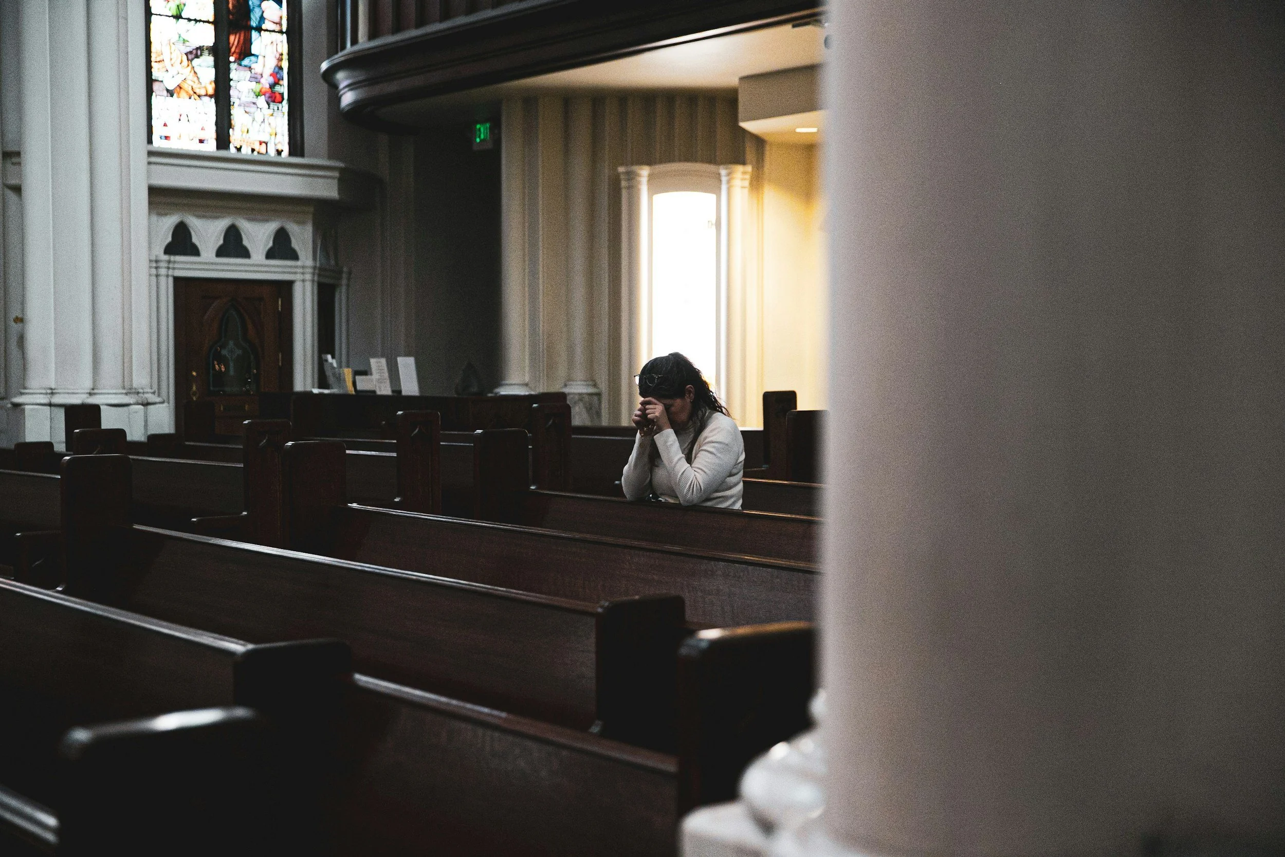 Woman sitting alone in a church pew with hands folded in prayer representing identity anchored in Christ beyond role during the empty nest season
