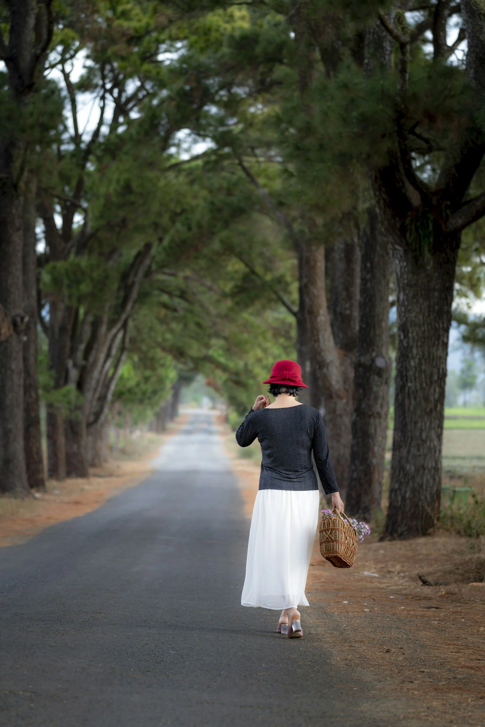 Middle aged woman in white dress and red hat walking away down a tree lined lane representing purpose dignity and forward motion in reclaiming identity in Christ