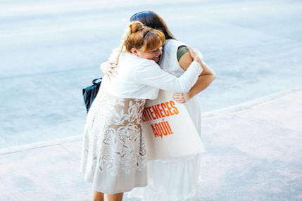 Mother and daughter hugging on a beach as the daughter holds a sign reading ‘You belong here,’ symbolizing identity, belonging, and love beyond roles.