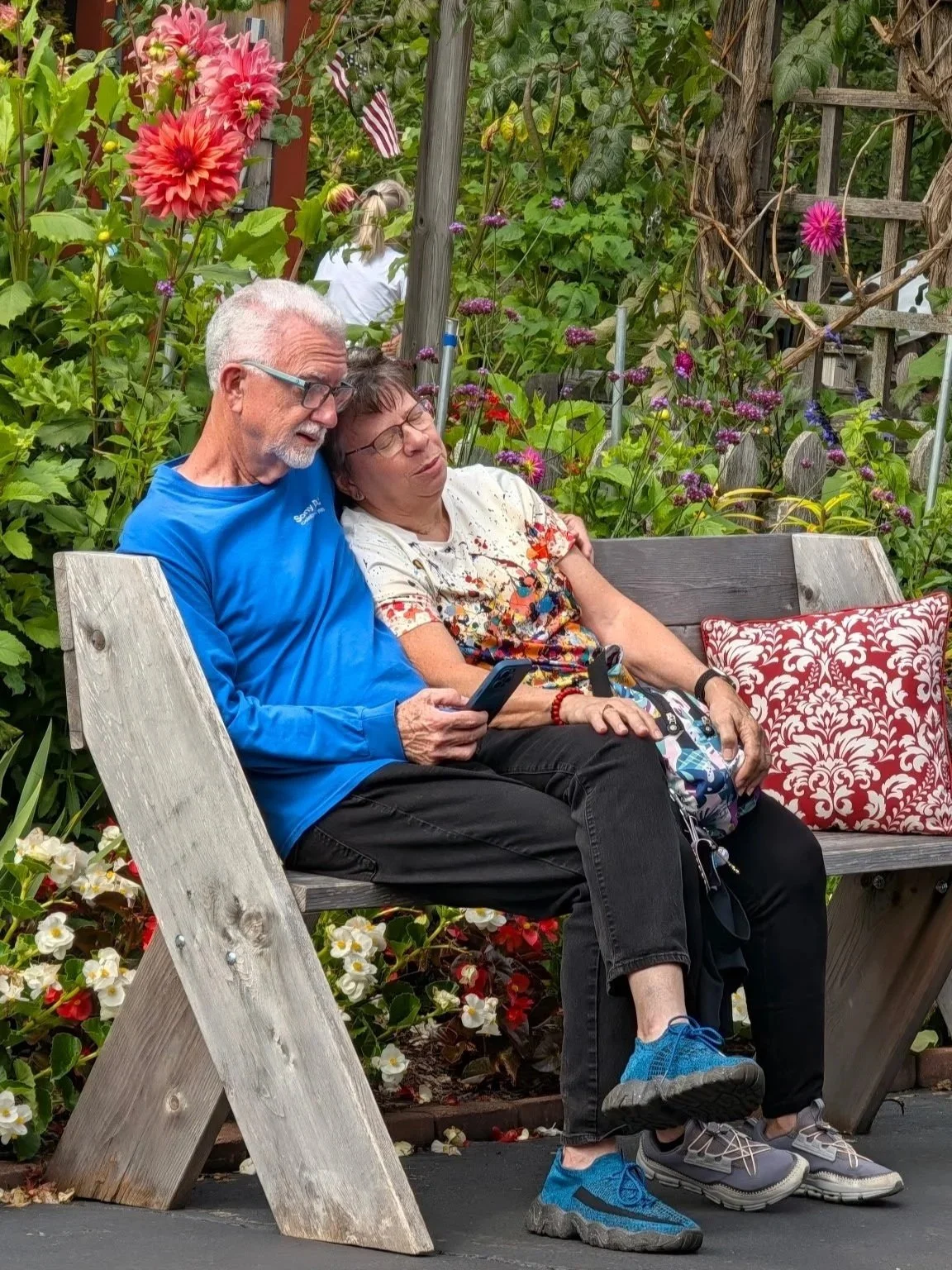 Jo and Beecher Wilhelm sitting together on a bench surrounded by flowers.