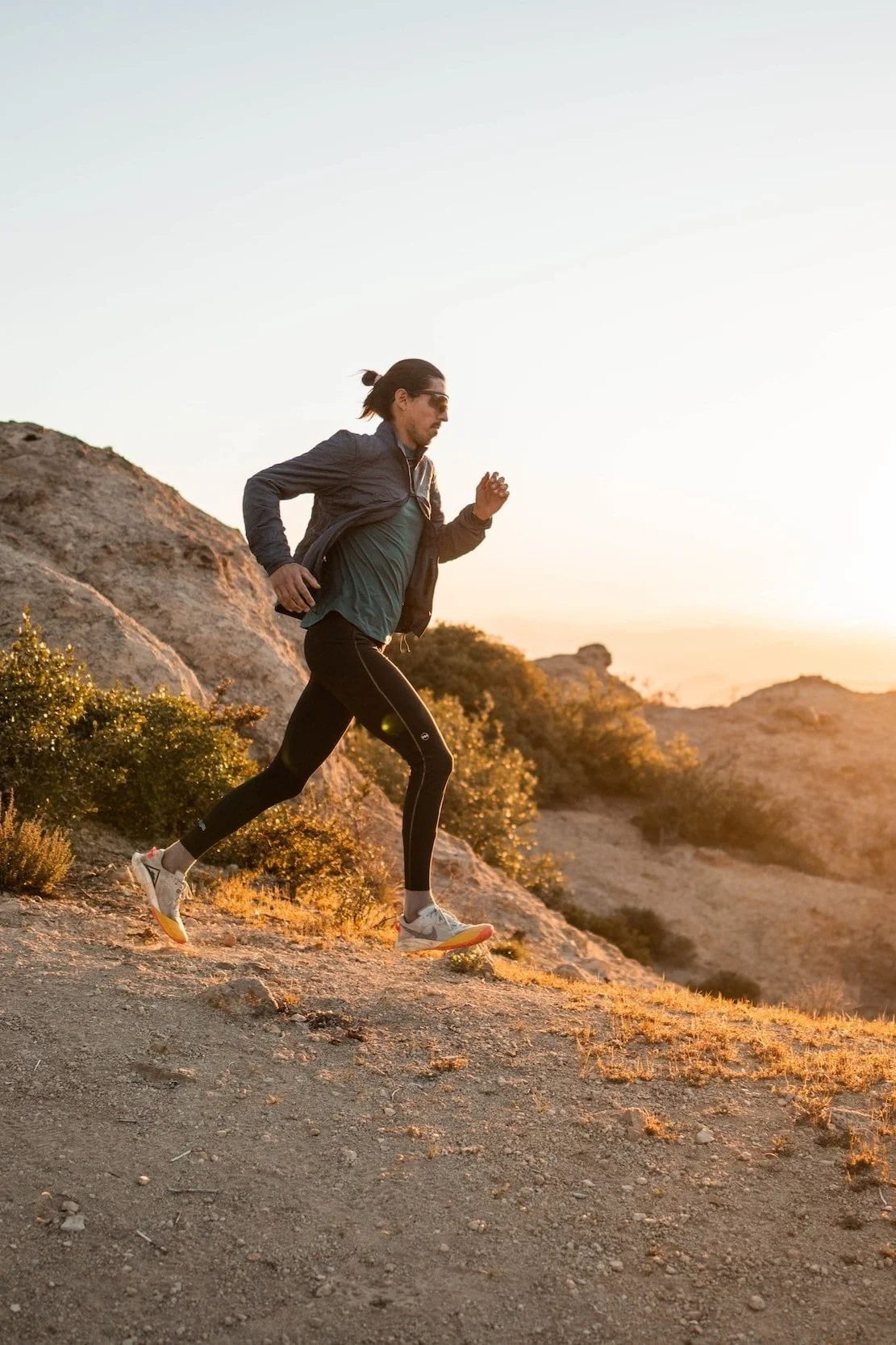 A man running on a dirt trail in a mountainous area during sunset.