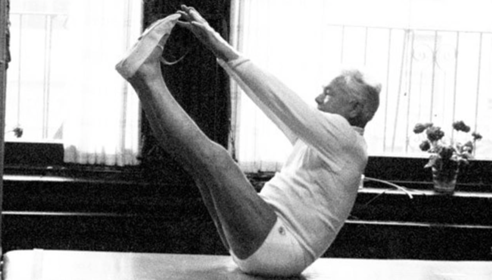 Joseph Pilates the creator of the Pilates Method performing a pose holding his feet with legs extended
