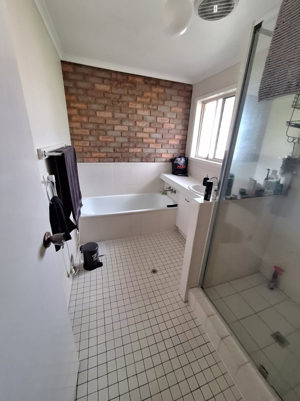 Bathroom with a bathtub, brick wall, white tiles, window, glass shower, and various toiletries.