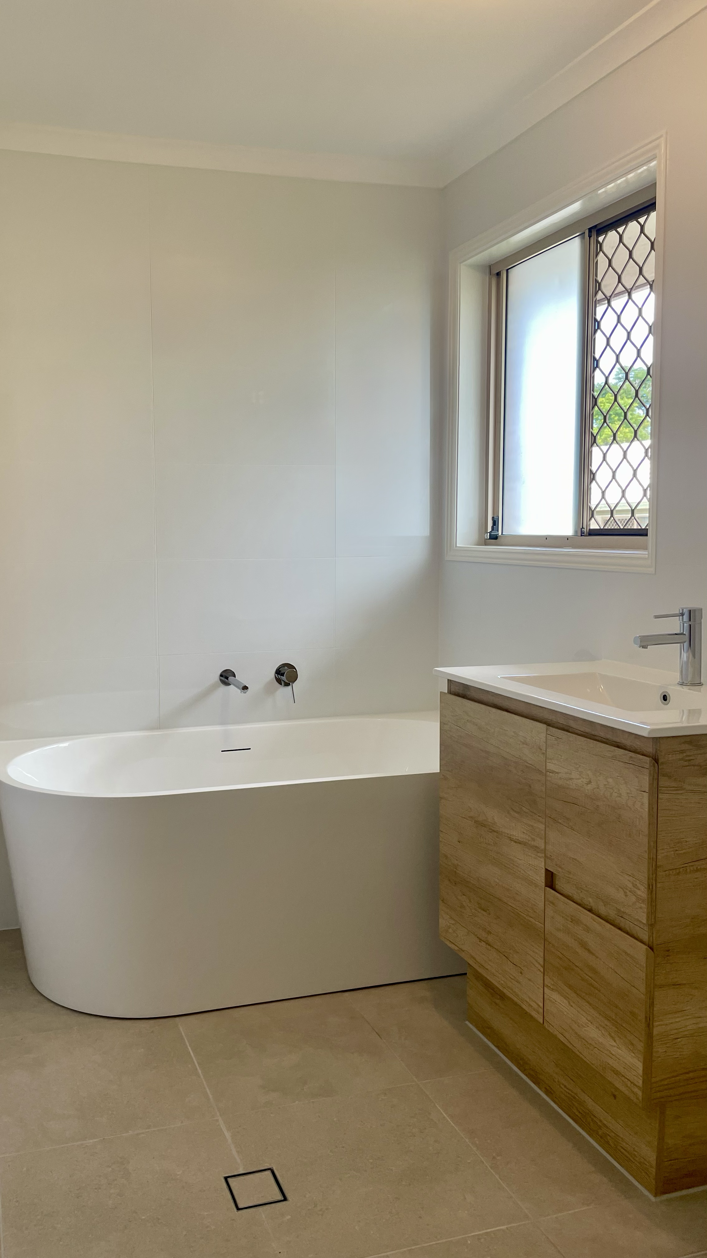 Bathroom renovation Rochedale South, Logan area, Brisbane Southside. Shower and modern vanity with round mirror, grey and white times. White bath tub, extra storage vertical cabinet.