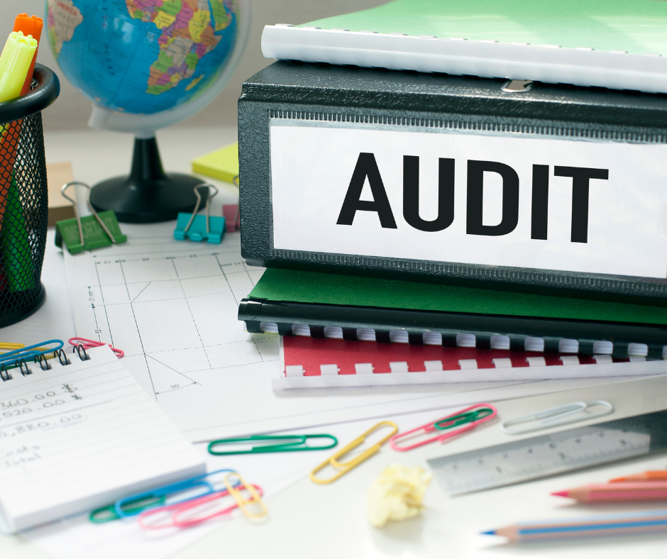 Office desk with an audit binder, papers, paper clips, a globe, and a notepad