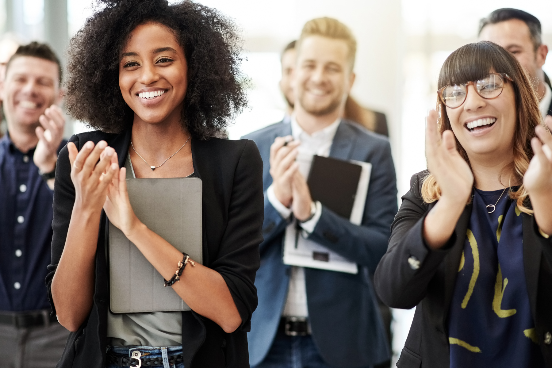 Group of diverse business professionals clapping and smiling at an event.