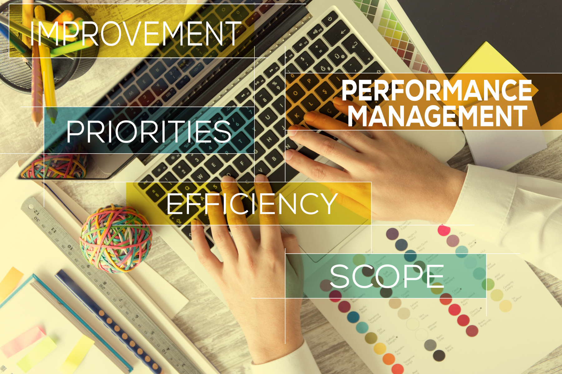 Hands typing on a laptop keyboard, surrounded by office supplies, color swatches, and words like "Improvement," "Priorities," "Efficiency," "Performance Management," and "Scope."