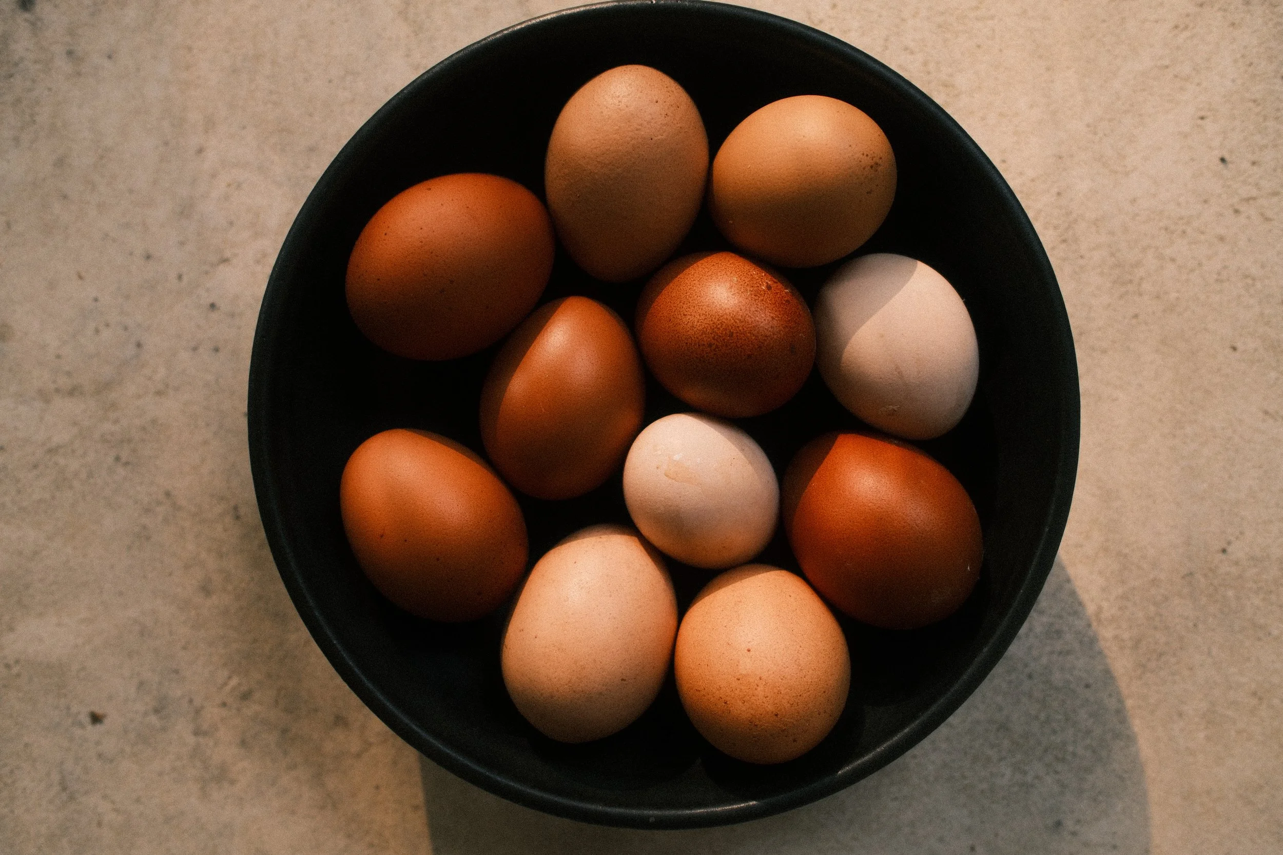A black bowl filled with a variety of brown and white eggs on a light-colored surface.