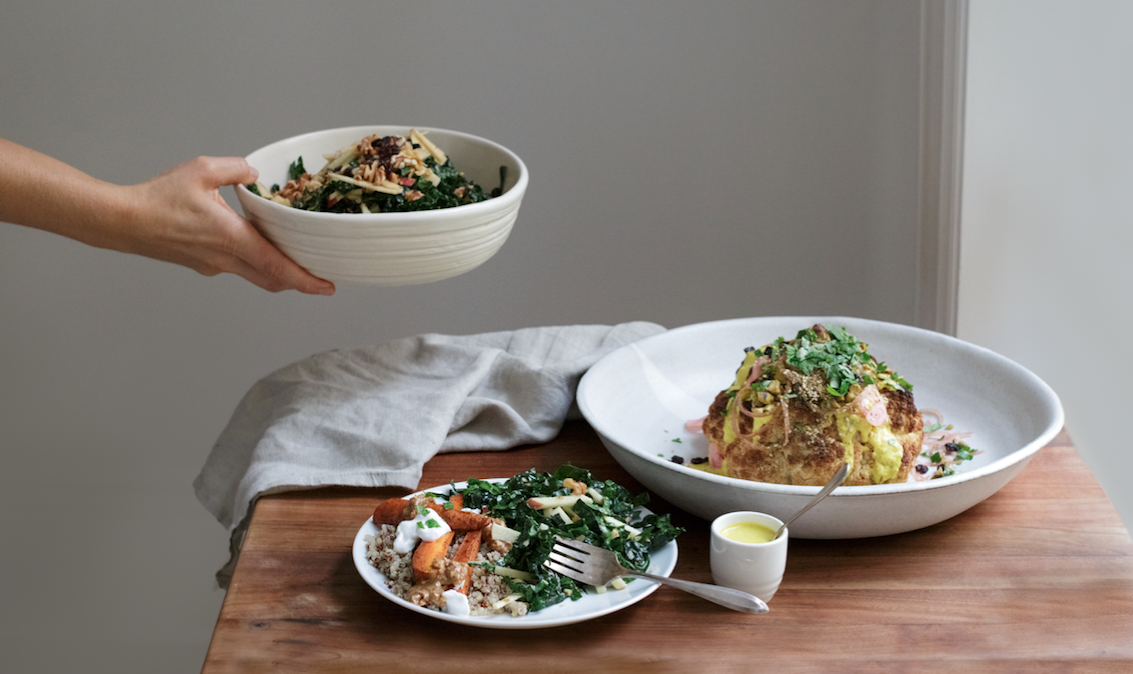 Person serving a bowl of salad to a table with a large plate of stuffed cabbage and a smaller plate of salad on a wooden surface.