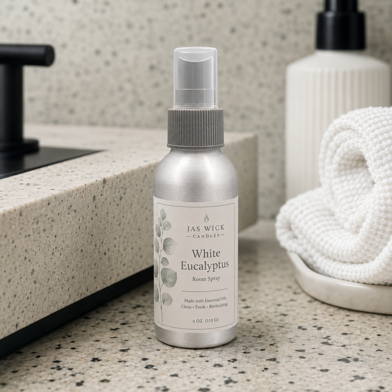 A small silver bottle of White Eucalyptus room spray on a countertop in a bathroom. Part of a vase with green plants and a bottle with a spray top are also visible.