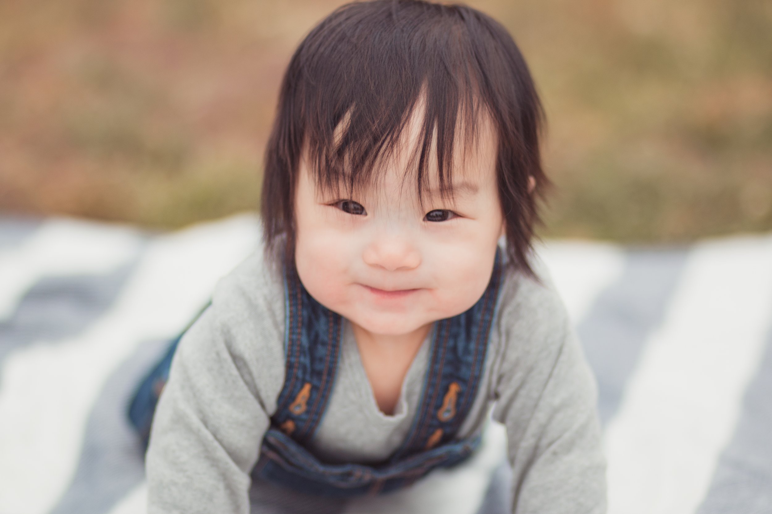Smiling toddler with dark hair crawling outdoors on a blanket.