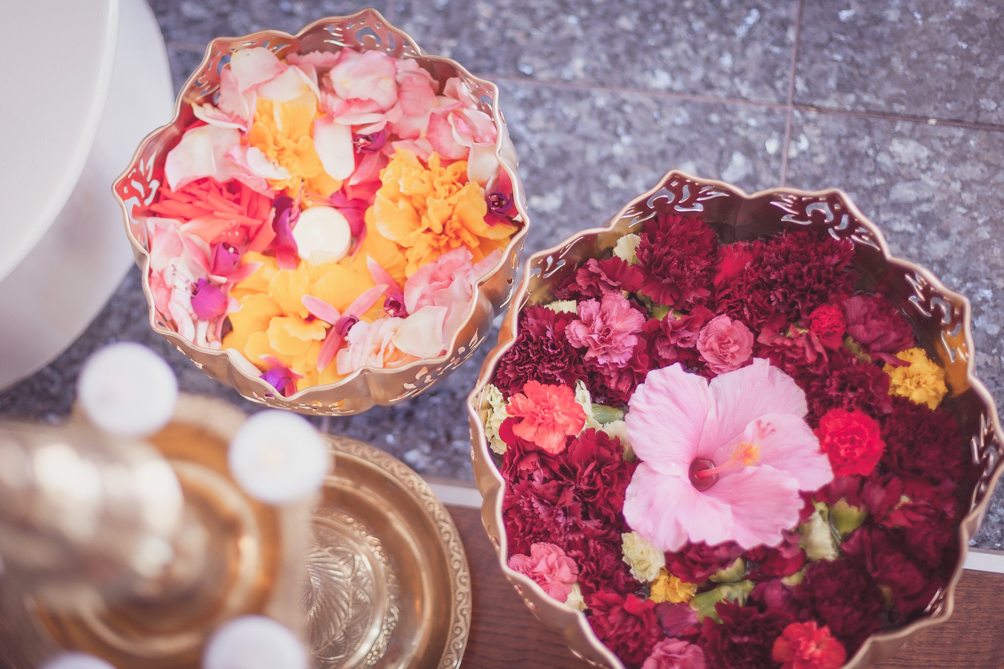 Decorative bowls filled with colorful flower petals, including pink, yellow, orange, and red, on a textured gray surface.