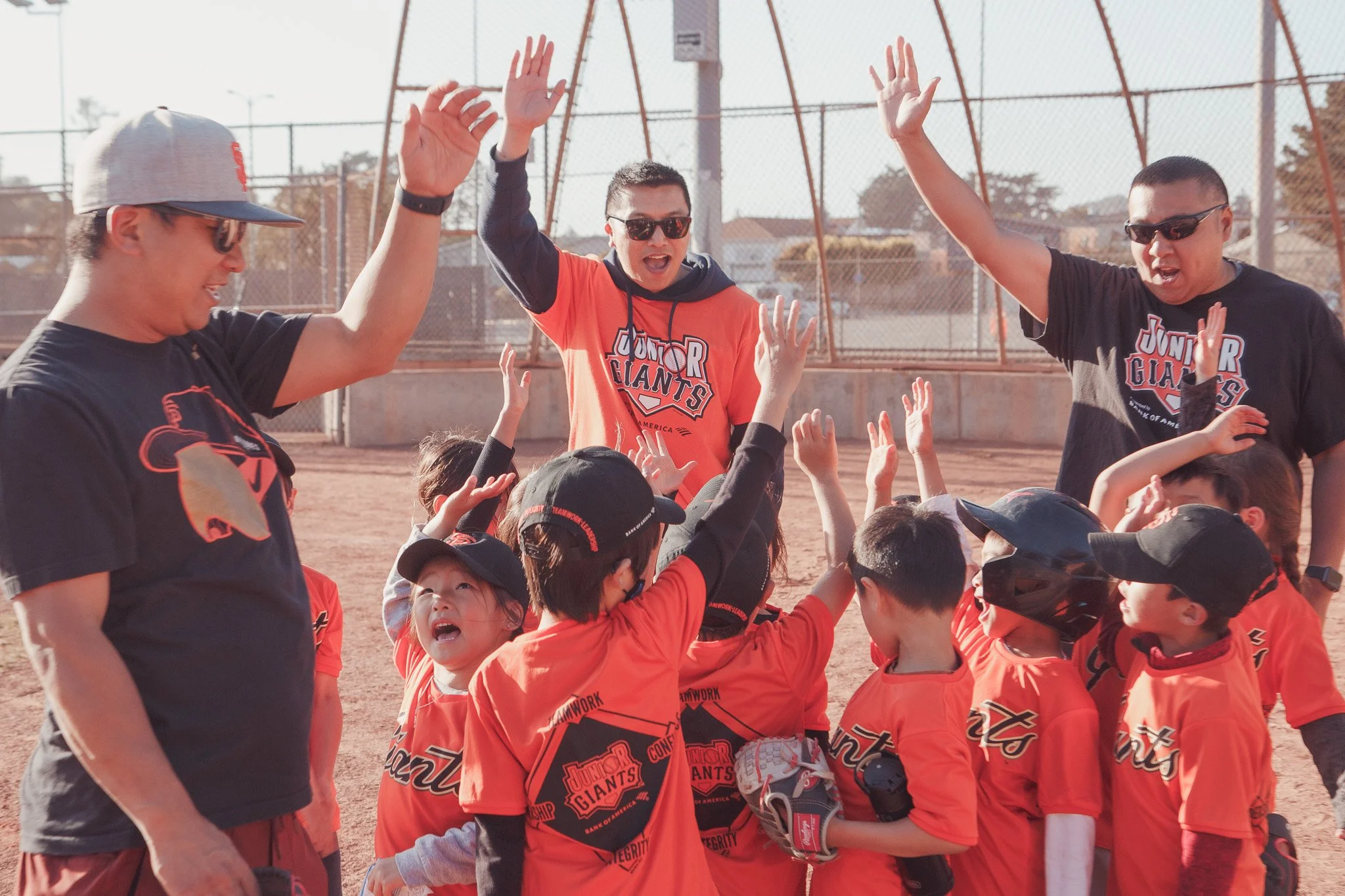 Youth baseball team with coaches celebrating and high-fiving on a dirt field.