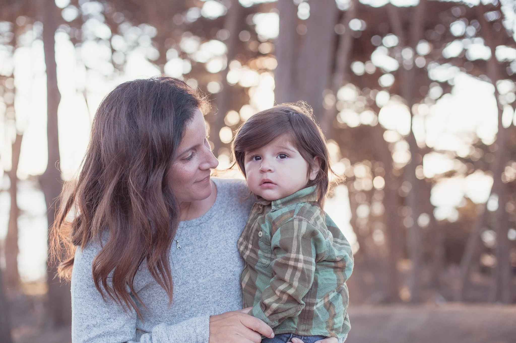 A woman holding a young boy outdoors with trees in the background during sunset.