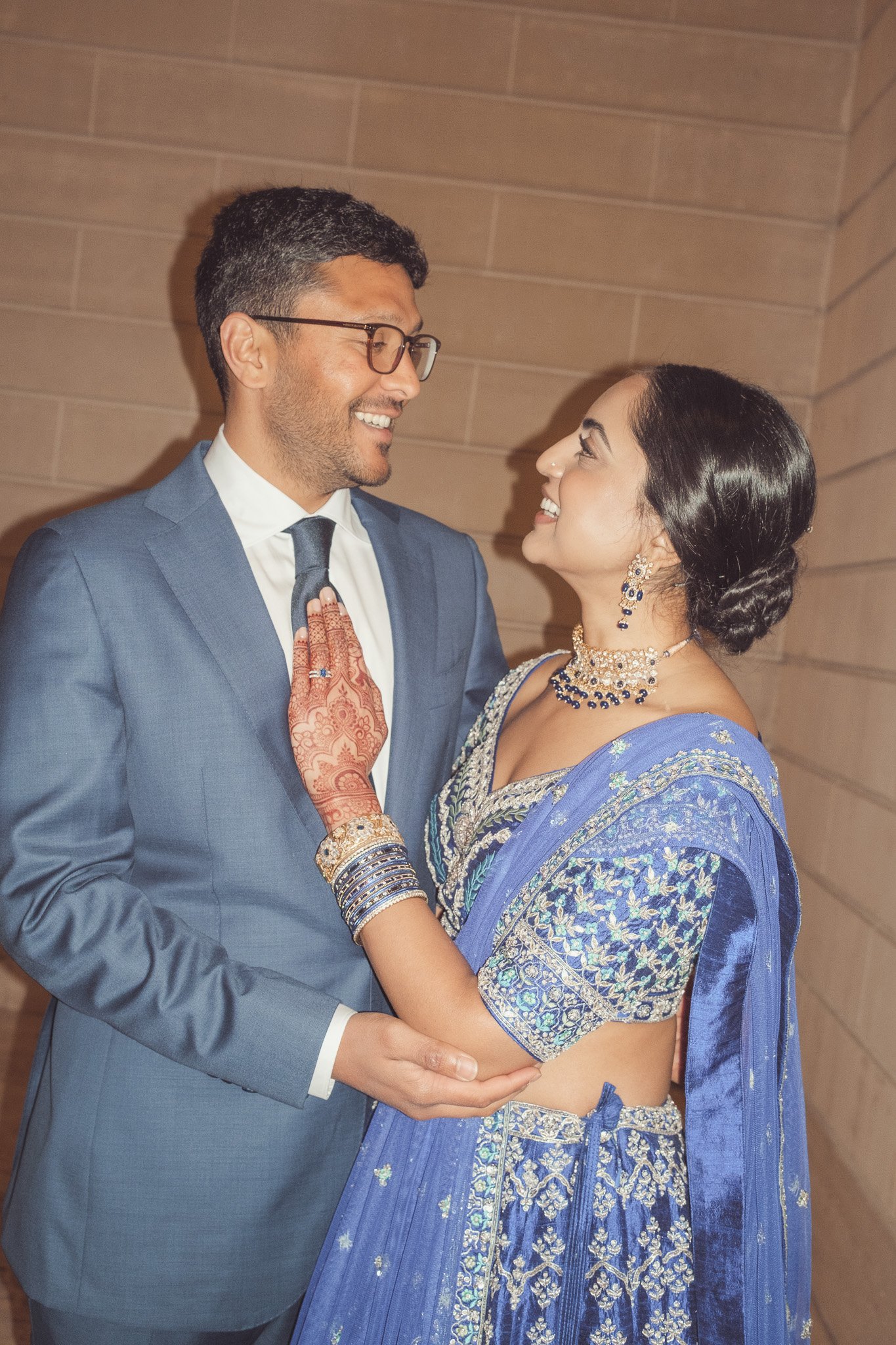 A man in a blue suit and a woman in a traditional blue Indian saree holding each other and smiling.