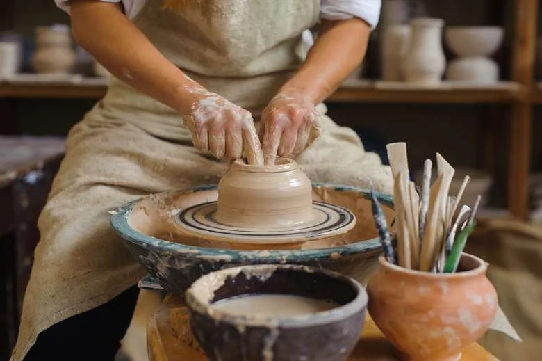 Person shaping a clay pot on a pottery wheel in a pottery studio.