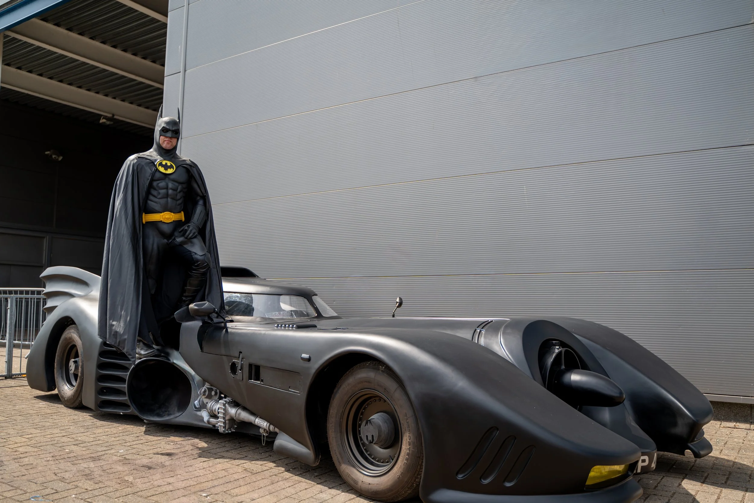 Batman cosplayer posing beside the 1989 Batmobile
