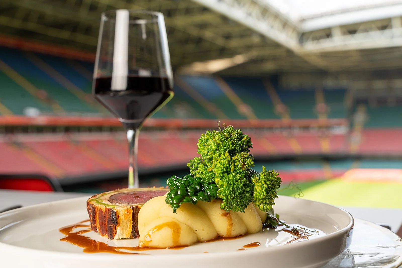 Plated beef dish with mashed potato and broccoli beside a glass of red wine at Principality Stadium in Cardiff.