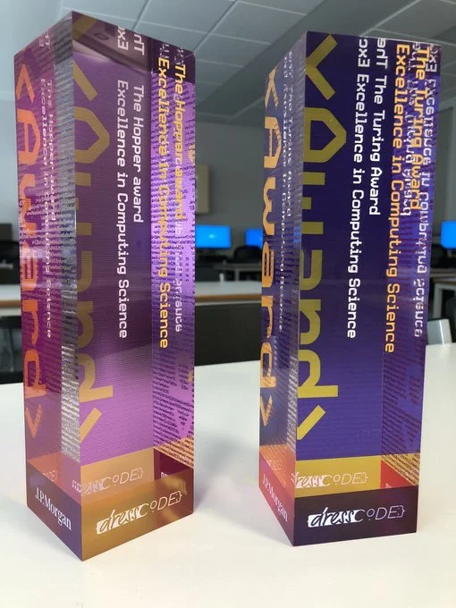 Two colorful award trophies for the Future of Work, Emerging in Cloud Science, and the Happiest Board. Each trophy has a purple background with text and a shiny design, placed on a white table with a blurred office setting in the background.