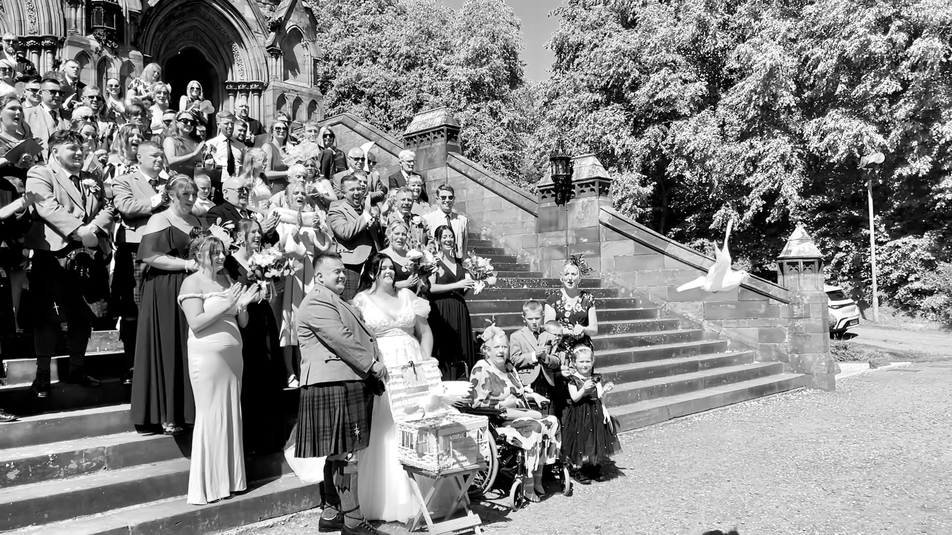 Bride and groom with wedding guests releasing white doves on the church steps in Glasgow, a touching moment to honour loved ones.
