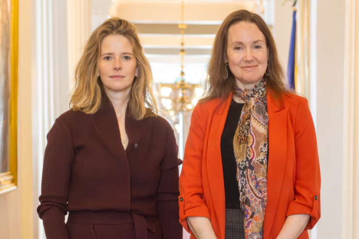 Two women standing inside a grand building with ornate decor, smiling at the camera.