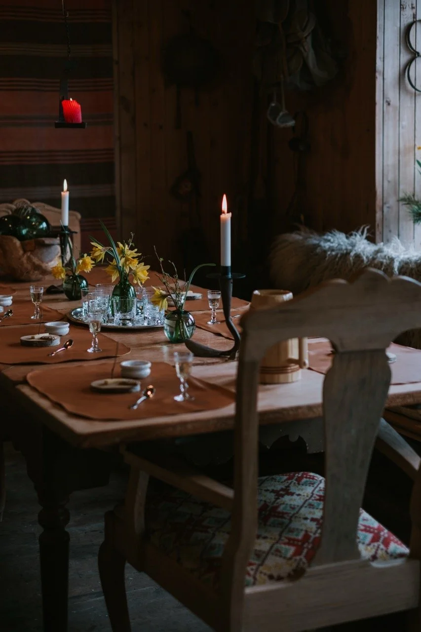 A rustic dining table with lit candles, yellow flowers, and tableware in a cozy cabin.
