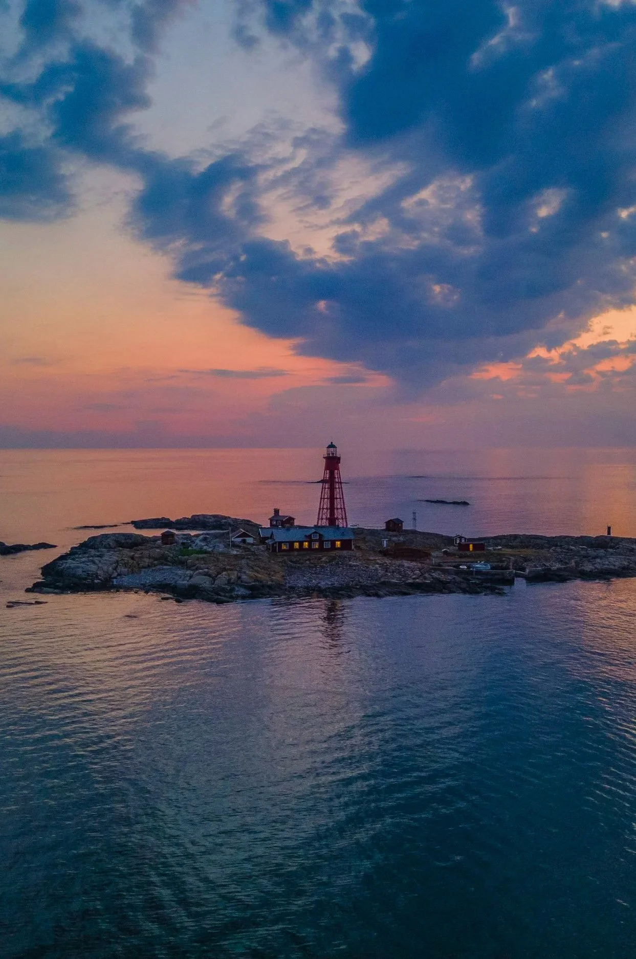 Aerial view of a small rocky island with a red lighthouse at sunset.