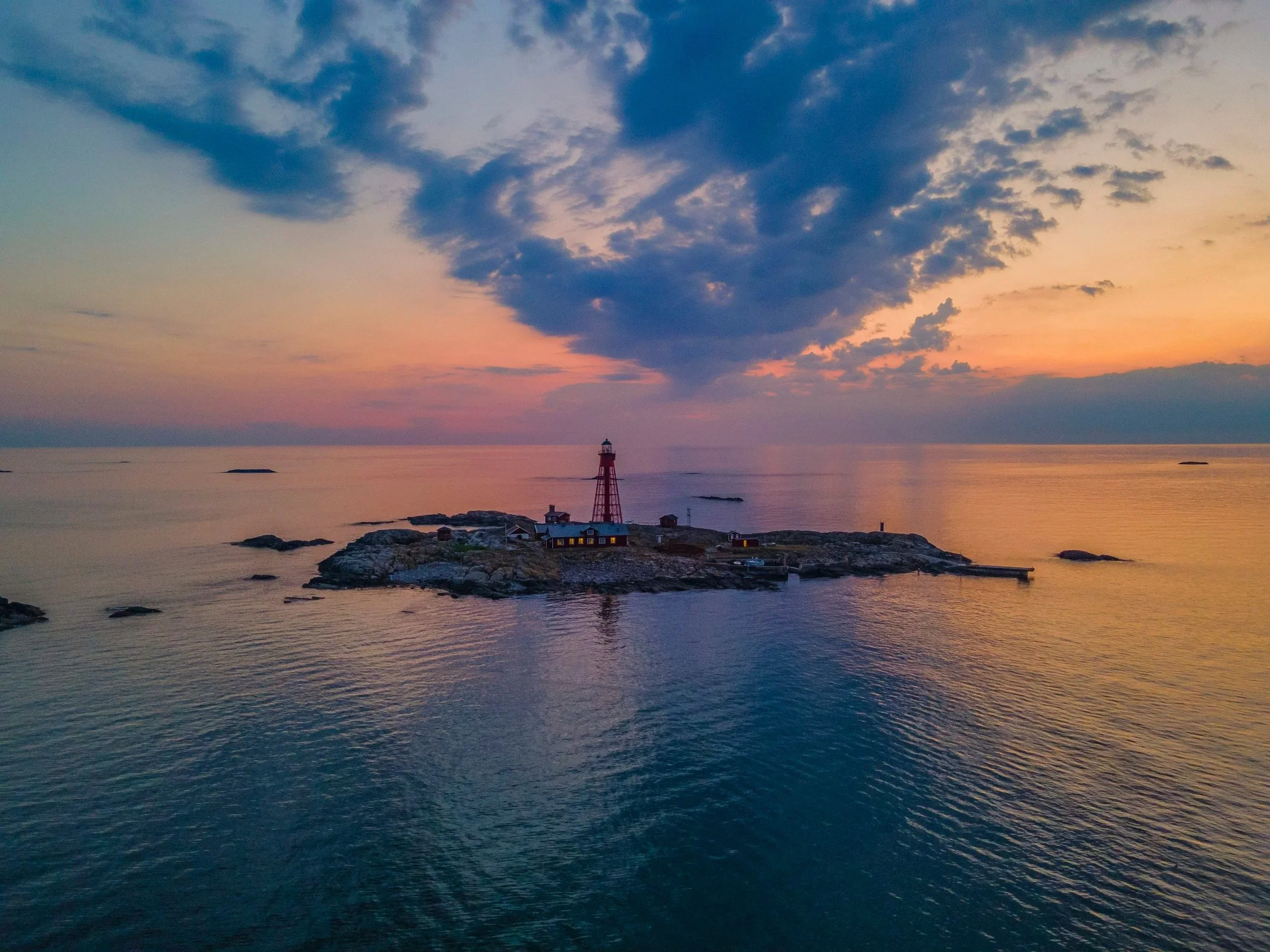 Aerial view of a small rocky island with a red lighthouse at sunset.