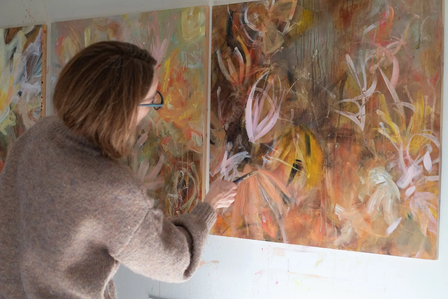 Person painting an abstract floral artwork on canvas in an art studio.