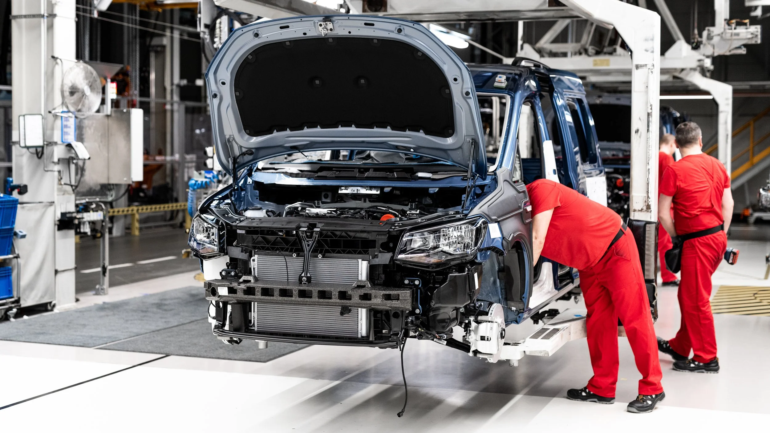 Mitarbeiter in roten Overalls reparieren eine Blue Volkswagen Transporter im Automobilwerk.