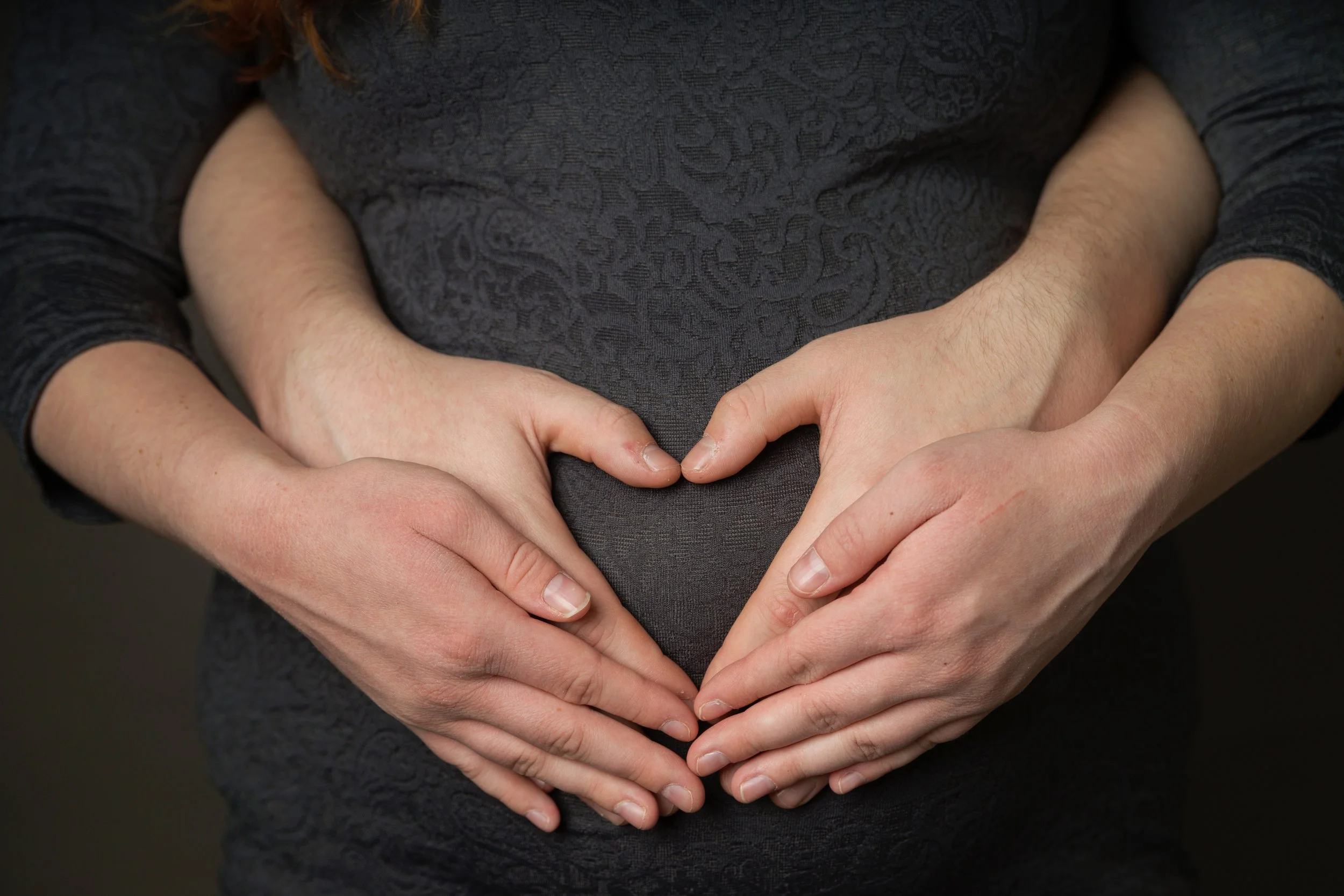 A pregnant woman forming a heart shape with her hands over her belly.