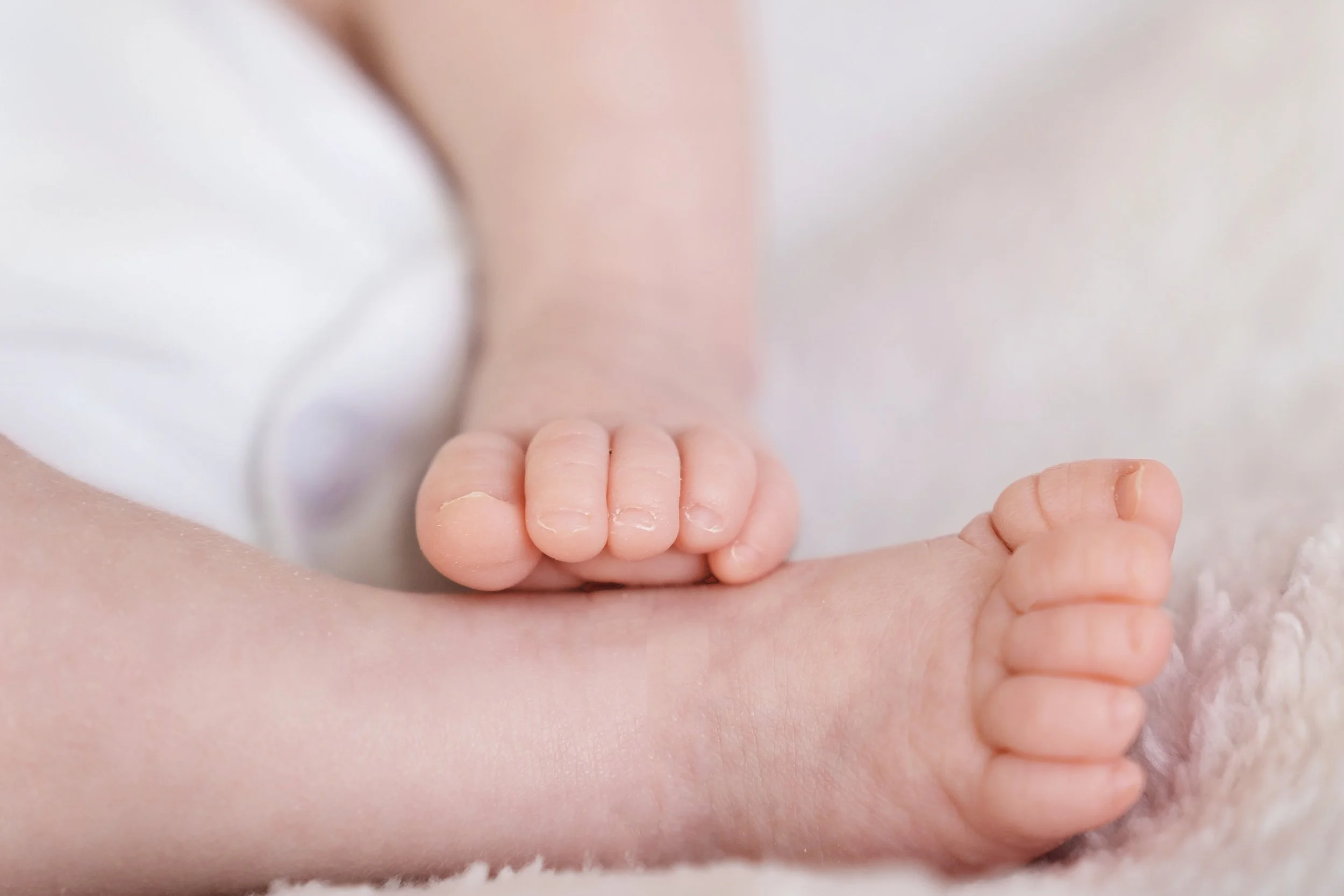 Close-up of a baby's hand resting on an adult's arm, with a soft blanket in the background.