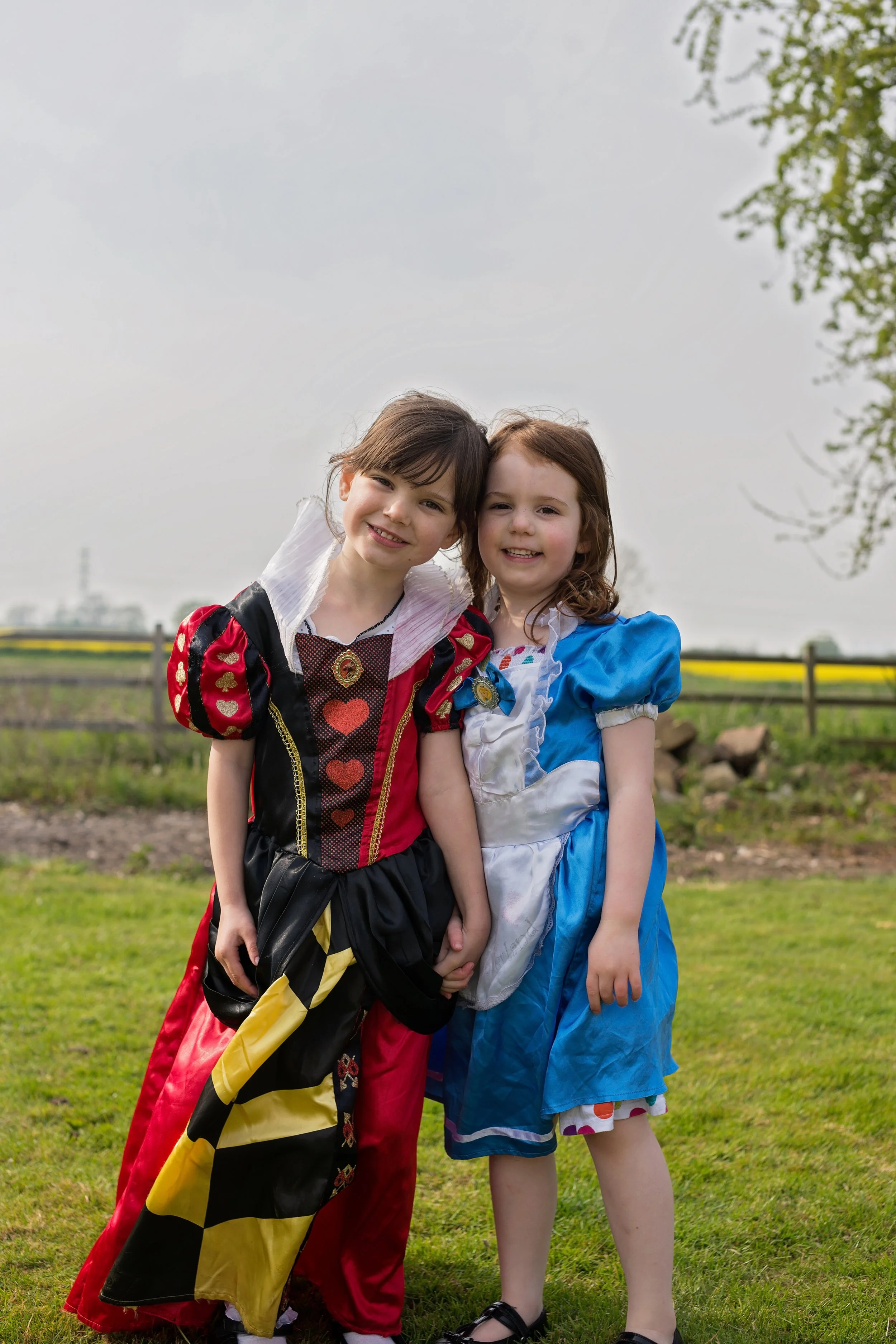 Two young girls dressed in colorful costumes standing outdoors on grass, smiling at the camera.