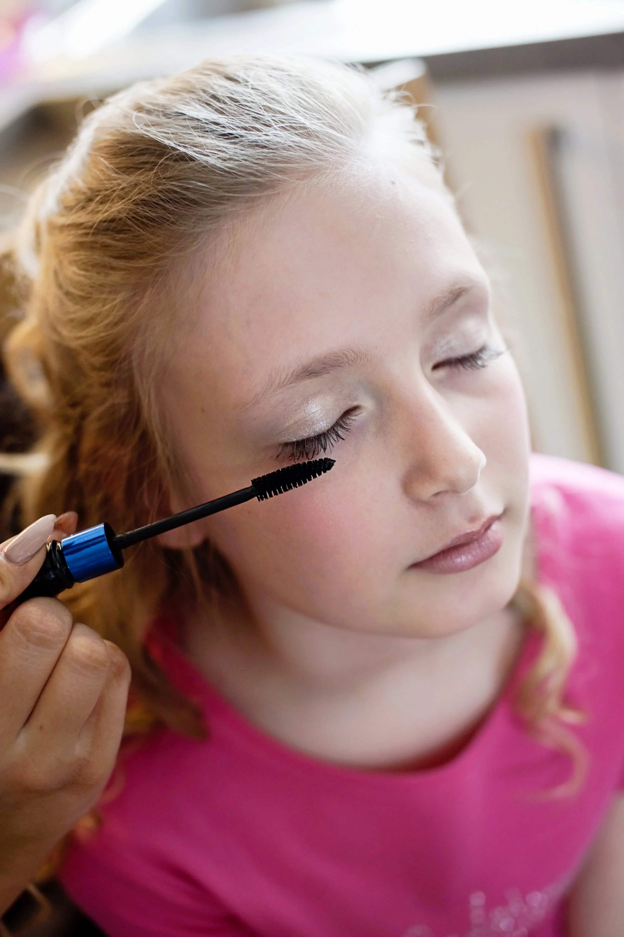 Young bridesmaid getting her make up done, she has her eyes closed and a mascara wand next to her eye