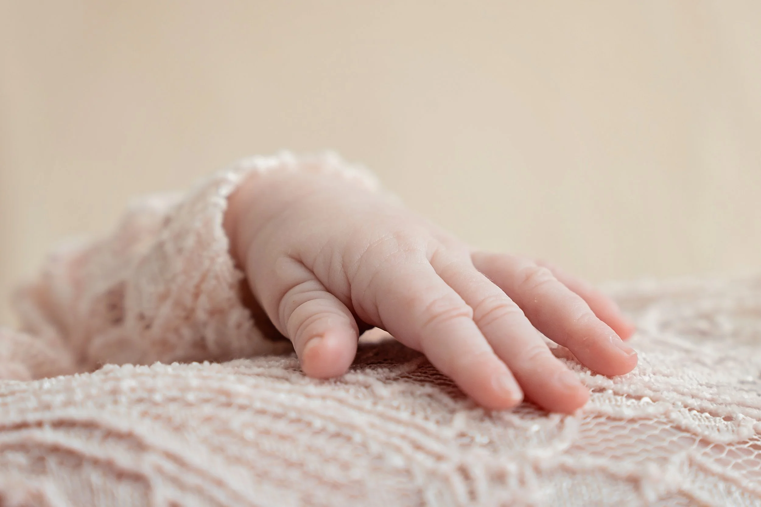 Close-up of a baby's hand resting on a soft, lacy fabric.